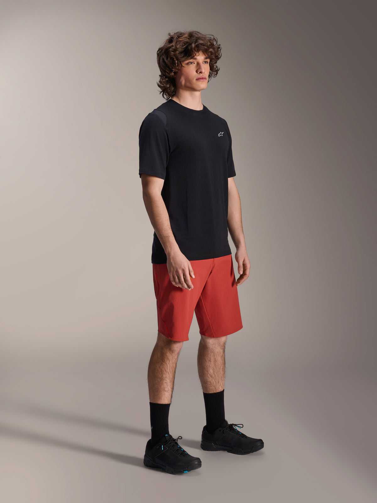 Męski model w spodenkach Alpinestars A-Dura Elite w kolorze Dark Orange i czarnej koszulce z krótkim rękawem A-Dura Dri Wool, odzież rowerowa MTB, czarne skarpety i buty, sportowy design do jazdy w terenie