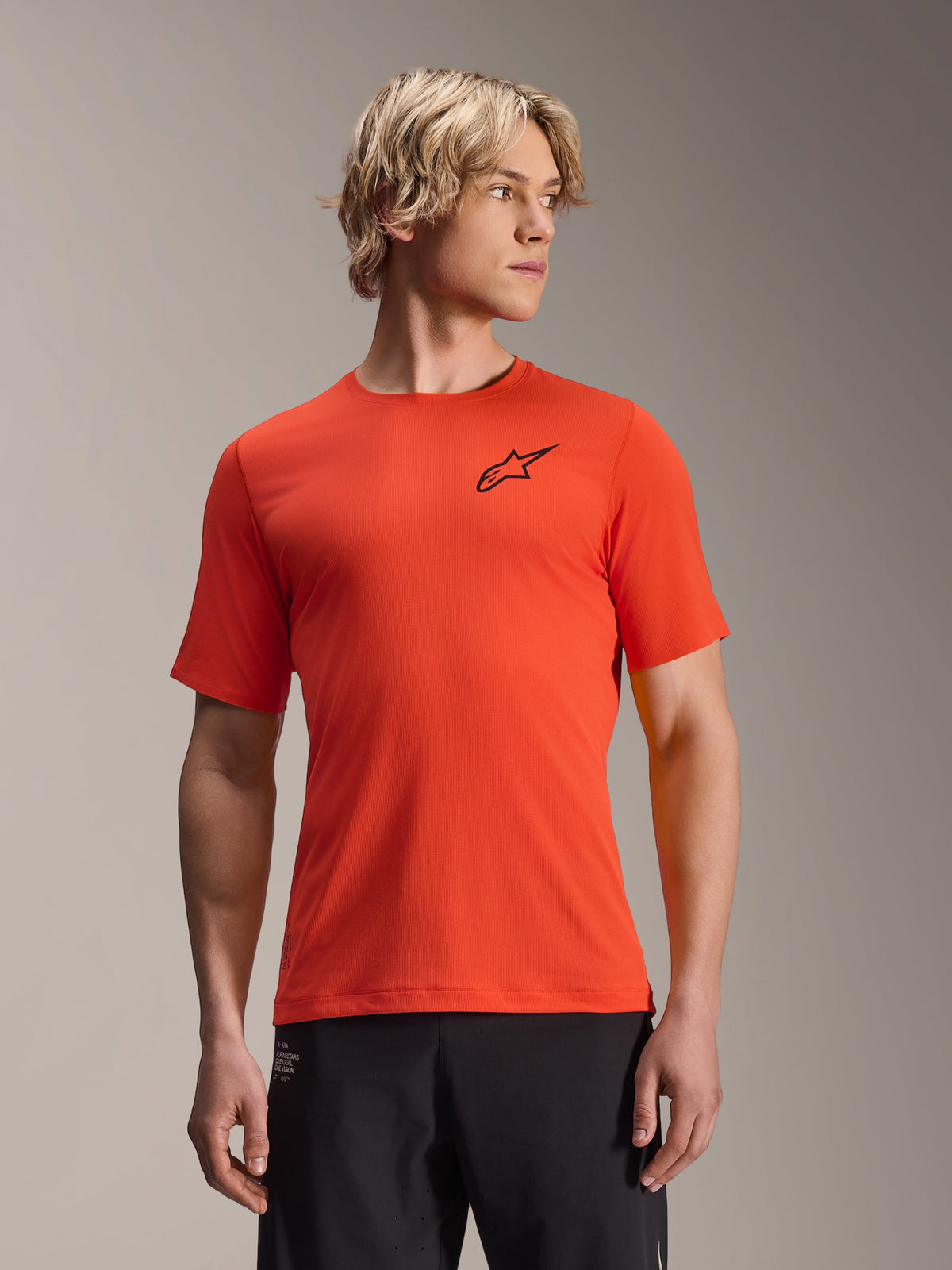 Alpinestars A-Aria Astar Short Sleeve Jersey, Spicy Orange with black star logo, Men's MTB mountain biking jersey, performance fit, worn by male model with blond hair and black pants