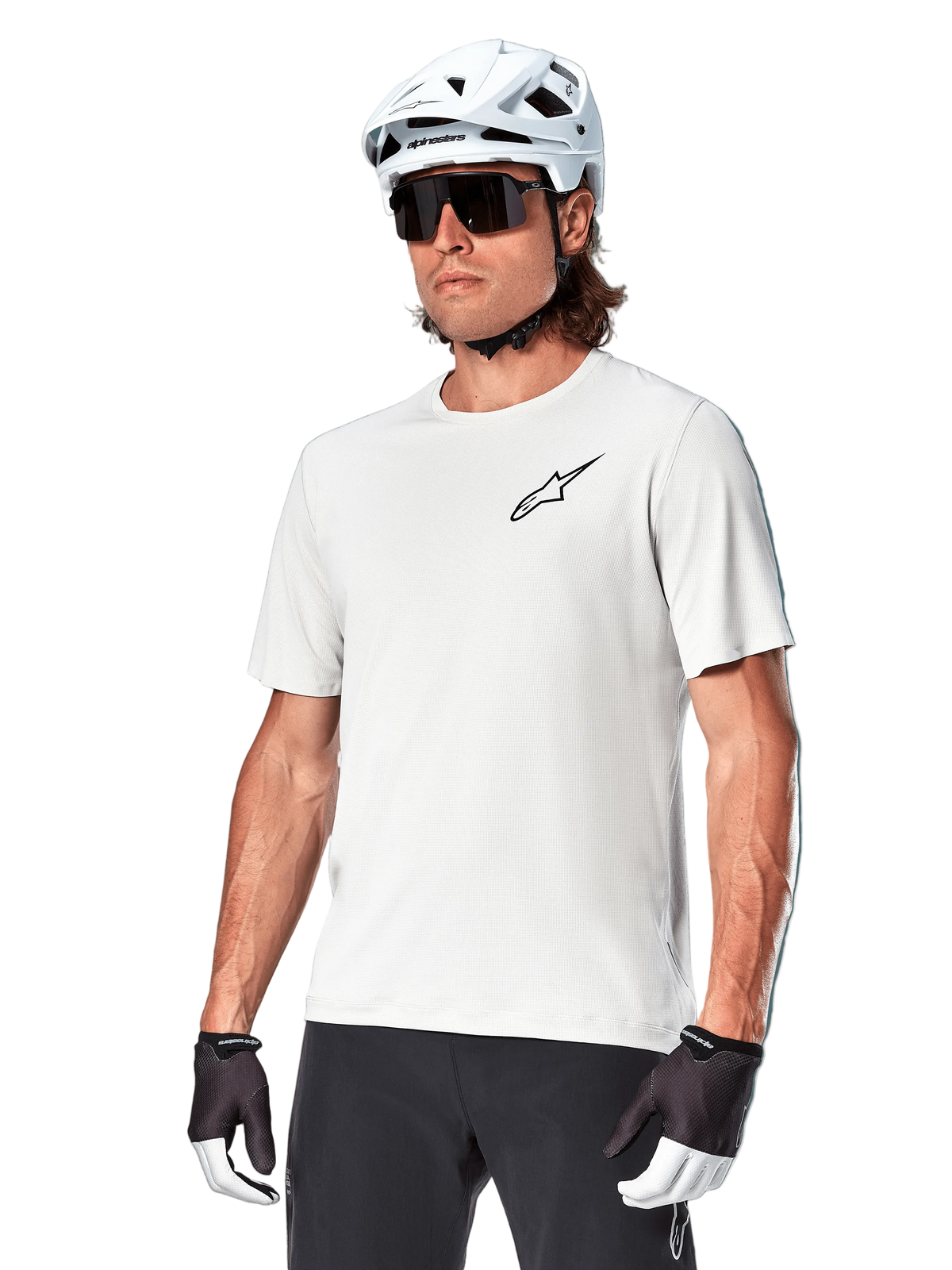 Alpinestars A-Aria Astar Short Sleeve Jersey, kolor White Dove, koszulka noszona przez rowerzystę w białym kasku i ciemnych okularach przeciwsłonecznych, małe czarne logo gwiazdy na piersi, oddychająca odzież wyczynowa do jazdy MTB