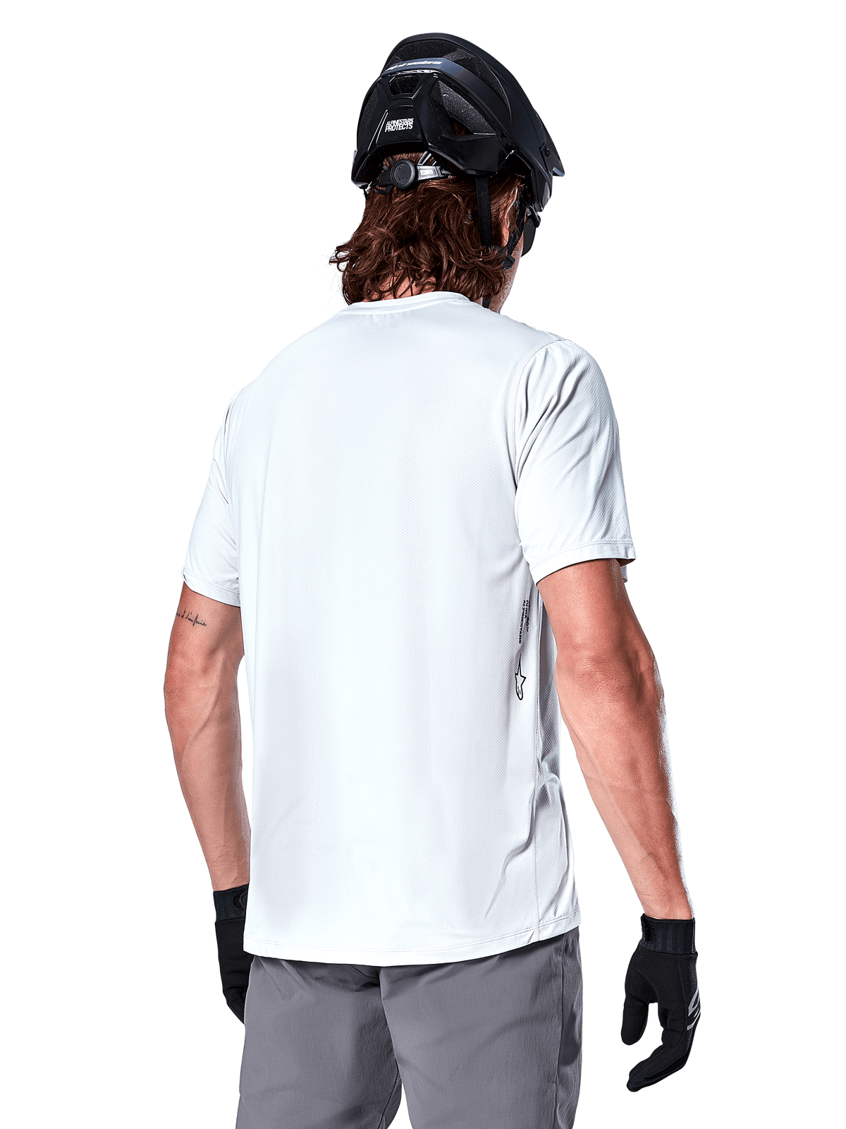 Alpinestars A-Dura Oscar Jersey, koszulka MTB z krótkim rękawem, biała (White Dove), widok od tyłu na rowerzystę w czarnym kasku, szarych szortach i czarnych rękawiczkach, techniczna odzież rowerowa