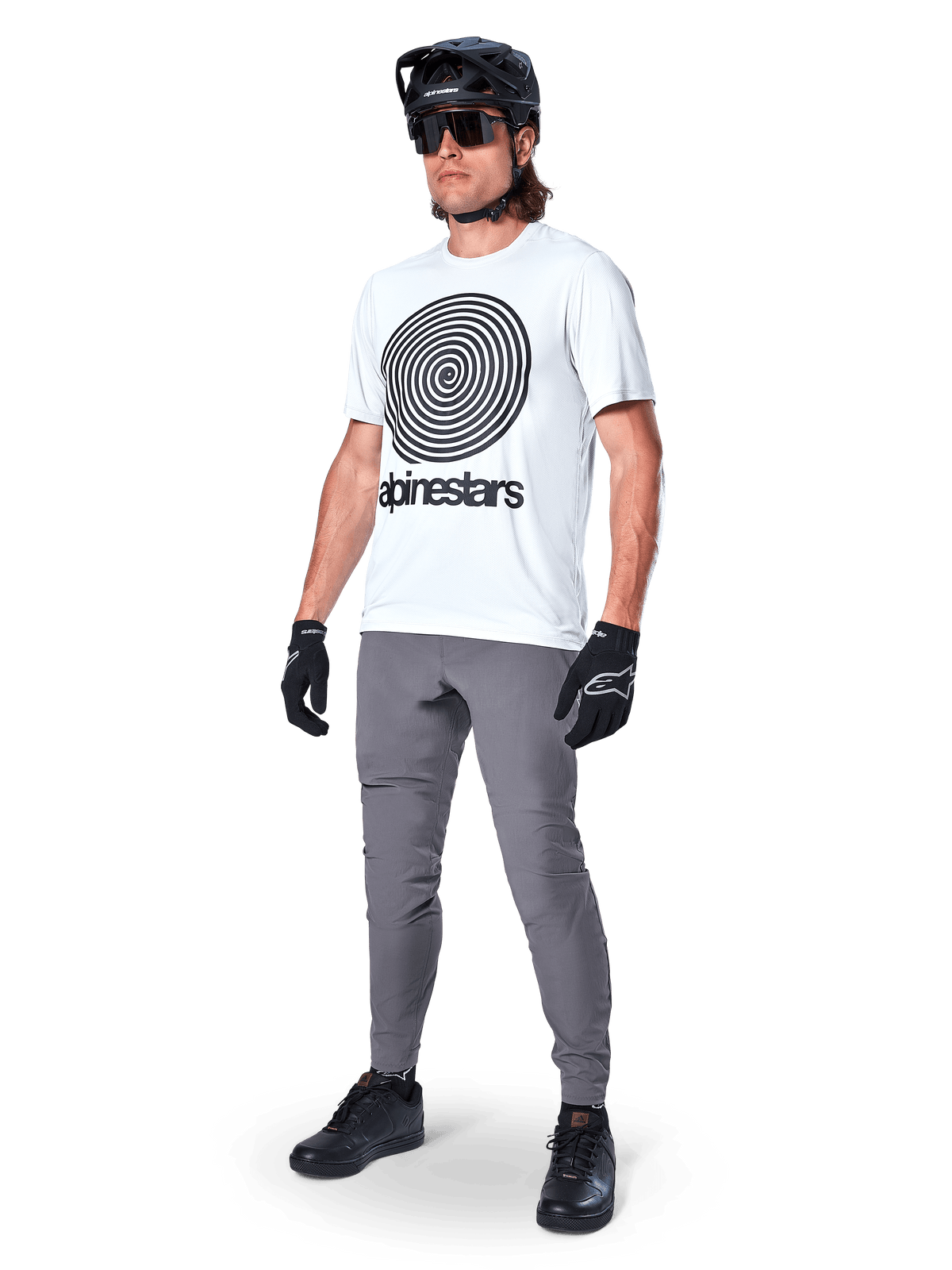 Koszulka Alpinestars A-Dura Oscar z krótkim rękawem, kolor White Dove z dużą czarną spiralną grafiką, noszona przez kolarza w szarych spodniach MTB, czarnym kasku i rękawiczkach, wydajna odzież rowerowa do jazdy w terenie