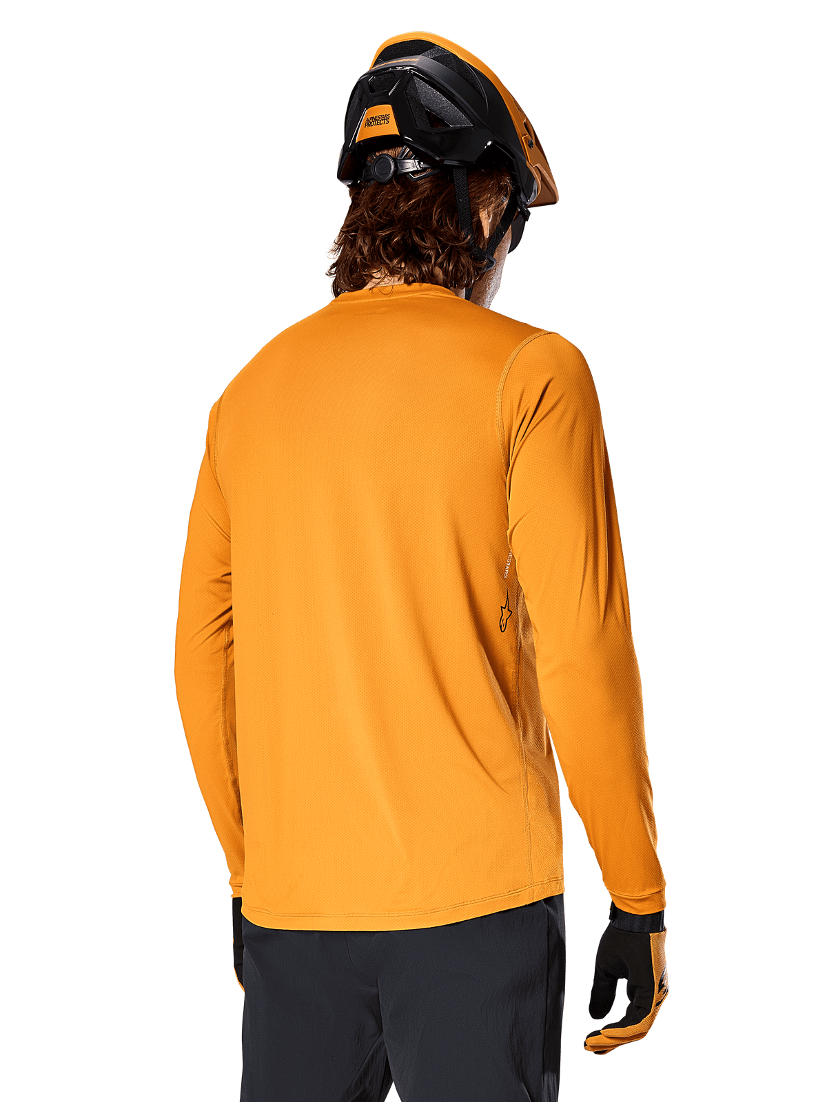 Alpinestars A-Dura Rocker Long Sleeve Jersey, ciemnozłoty, widok z tyłu na rowerzystę ubranego w czarno-pomarańczowy kask MTB, ciemne spodnie i dopasowane rękawiczki, swobodna odzież do kolarstwa górskiego
