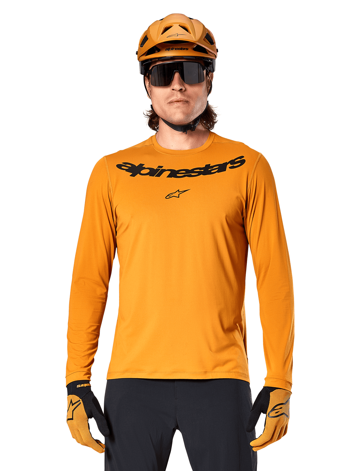 Koszulka z długim rękawem Alpinestars A-Dura Rocker w kolorze ciemnozłotym, z czarnym logotypem na piersi, noszona z pasującym złotym kaskiem i rękawicami do jazdy na rowerze górskim.