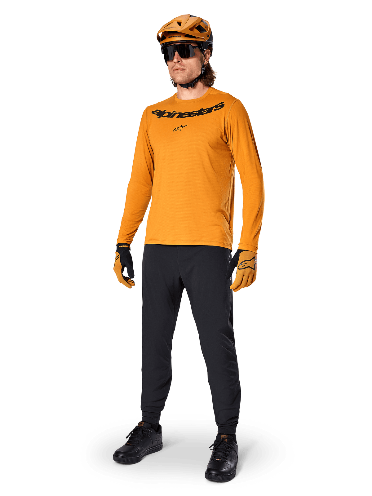 Koszulka z długim rękawem Alpinestars A-Dura Rocker, kolarska koszulka w kolorze Dark Gold, noszona z dopasowanym kaskiem MTB i czarnymi spodniami, z czarnym logotypem na klatce piersiowej, skoordynowana odzież wyczynowa do jazdy terenowej na rowerze górskim