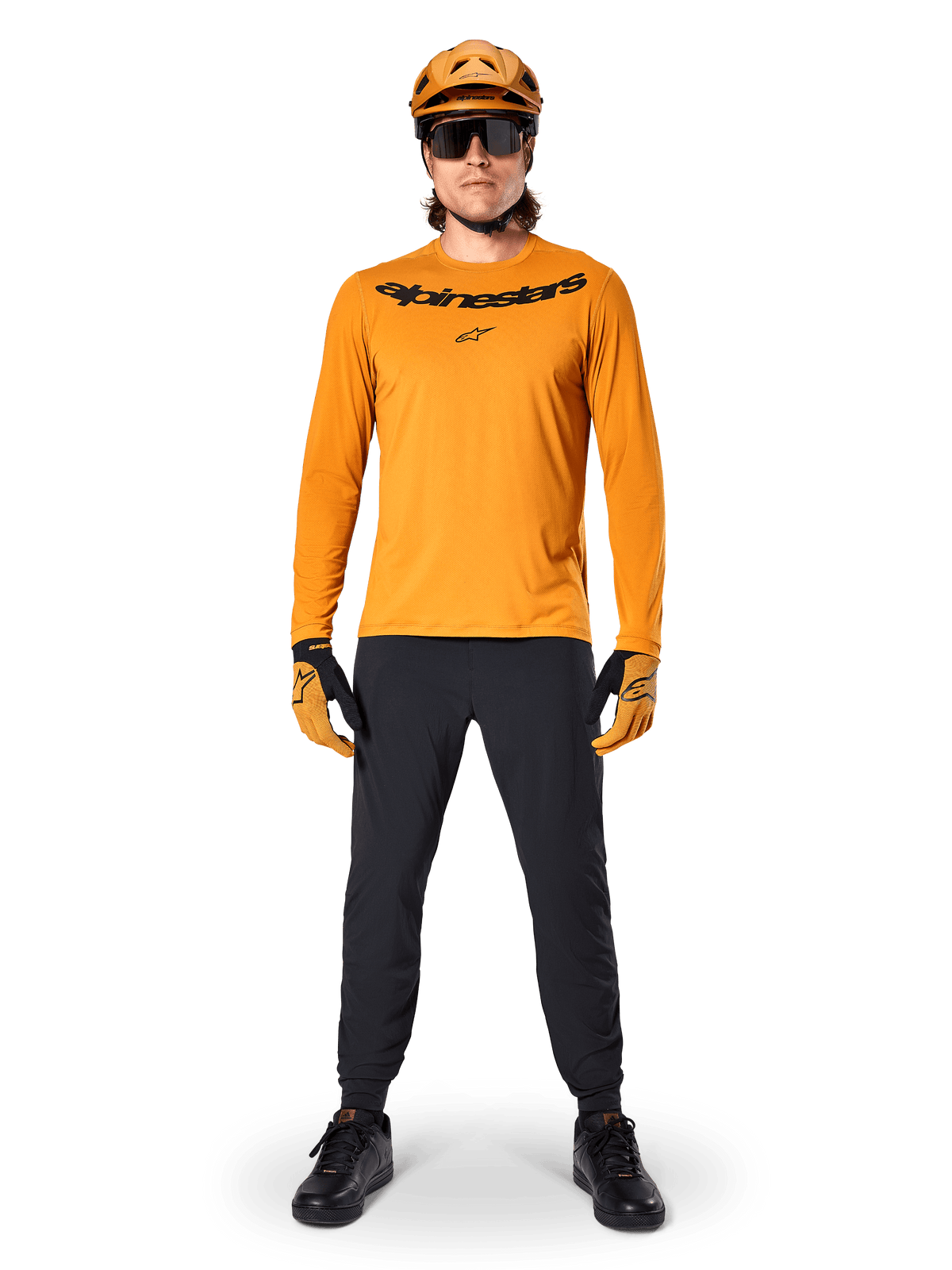 Koszulka z długim rękawem Alpinestars A-Dura Rocker w kolorze ciemnozłotym, z czarnym logo na piersi, w zestawie z dopasowanym złotym kaskiem MTB, czarnymi okularami przeciwsłonecznymi i czarnymi spodniami, profesjonalny strój do kolarstwa górskiego