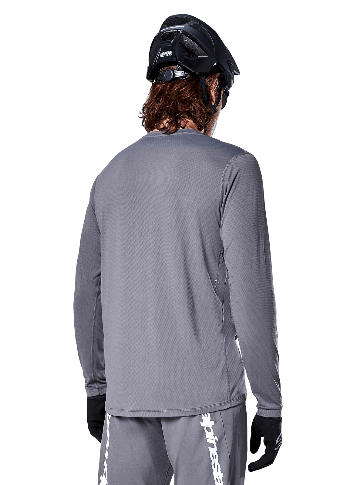 Alpinestars A-Dura Rocker Long Sleeve Jersey, ciemnoszara koszulka rowerowa z długim rękawem, widok kolarza górskiego od tyłu, pasujące szare spodenki z białym logo, czarny kask MTB i czarne rękawiczki, profesjonalna odzież do kolarstwa terenowego