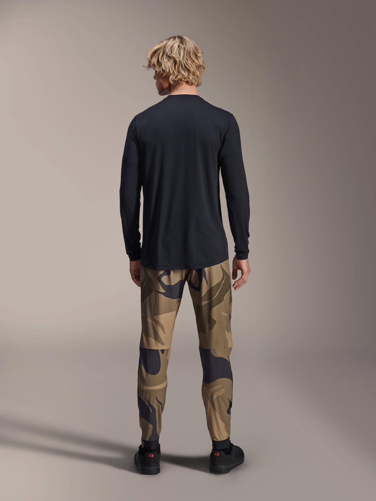 Alpinestars A-Dura Camo Pant, Mountain Bike Pants, Brown Camouflage pattern, rear view, worn with a black long-sleeve jersey and black sneakers, regular fit textile pants for off-road cycling