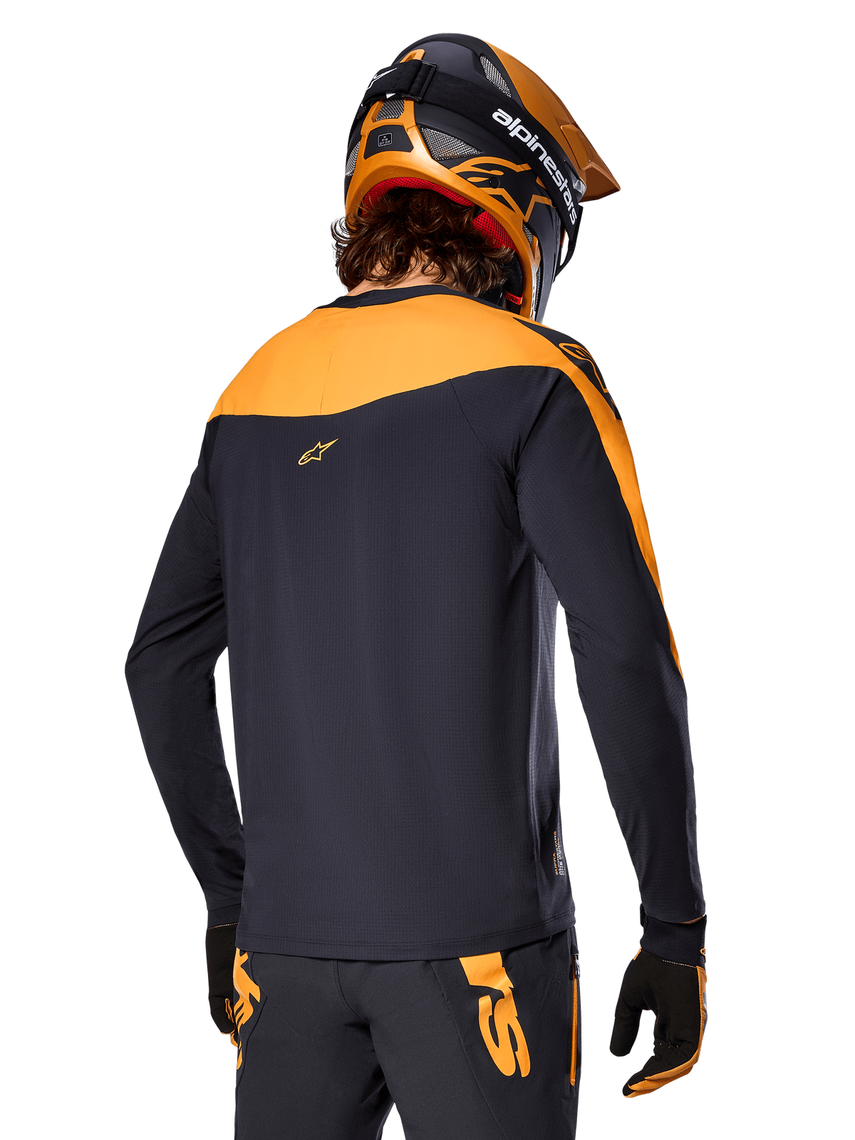 Alpinestars A-Supra Race Jersey - Long Sleeve, czarno-pomarańczowa, widok z tyłu na rowerzystę w pasującym kasku i spodniach MTB, sportowy krój z mikroperforowaną teksturą, profesjonalny strój wyścigowy MTB