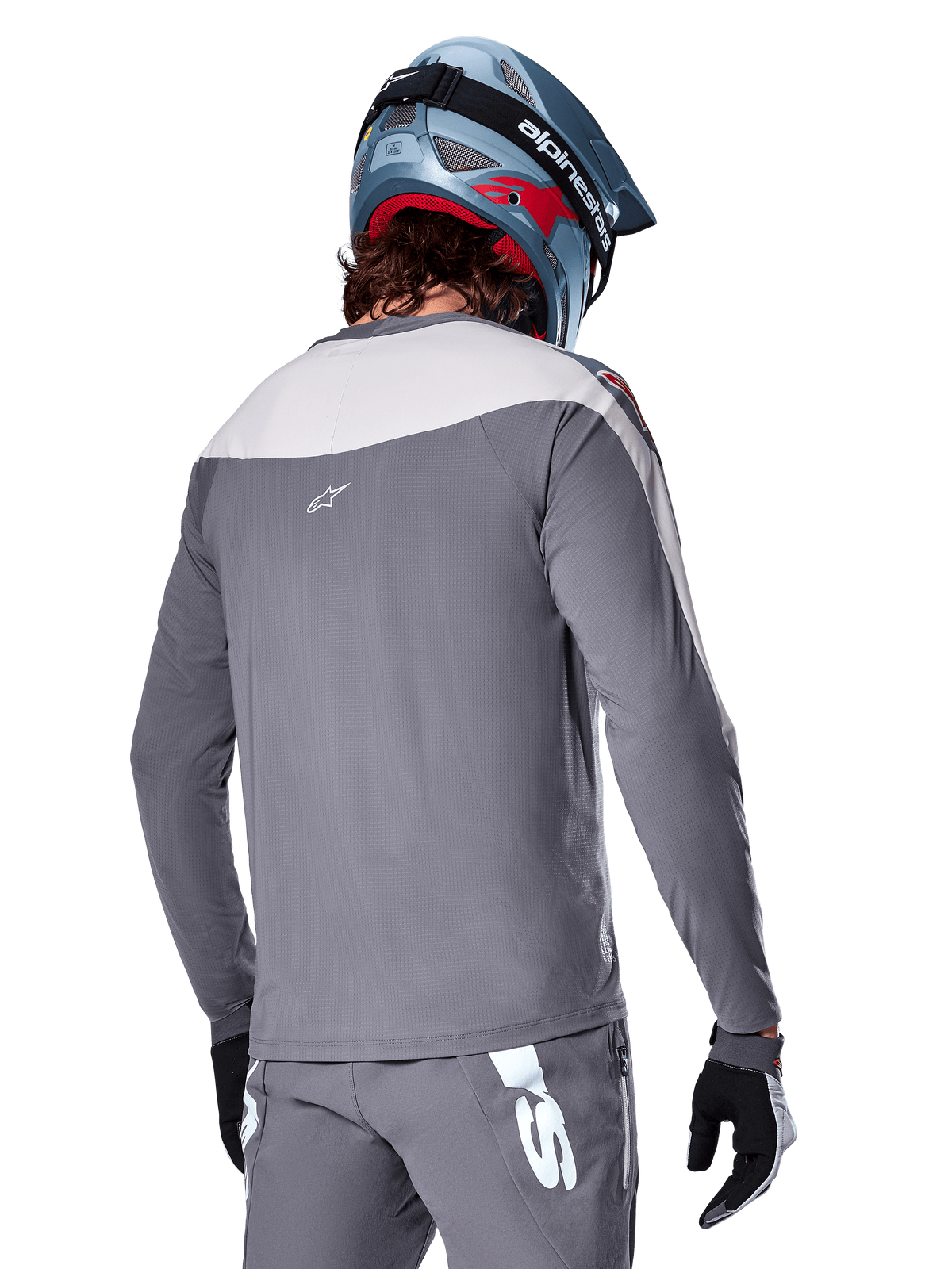 Koszulka Alpinestars A-Supra Race, koszulka MTB z długim rękawem w kolorze ciemnoszarym i jasnoszarym, widok z tyłu ukazujący sportowy krój i logo Astar, noszona z pasującymi szarymi spodniami i niebieskim kaskiem rowerowym, zaprojektowana do jazdy terenowej MTB