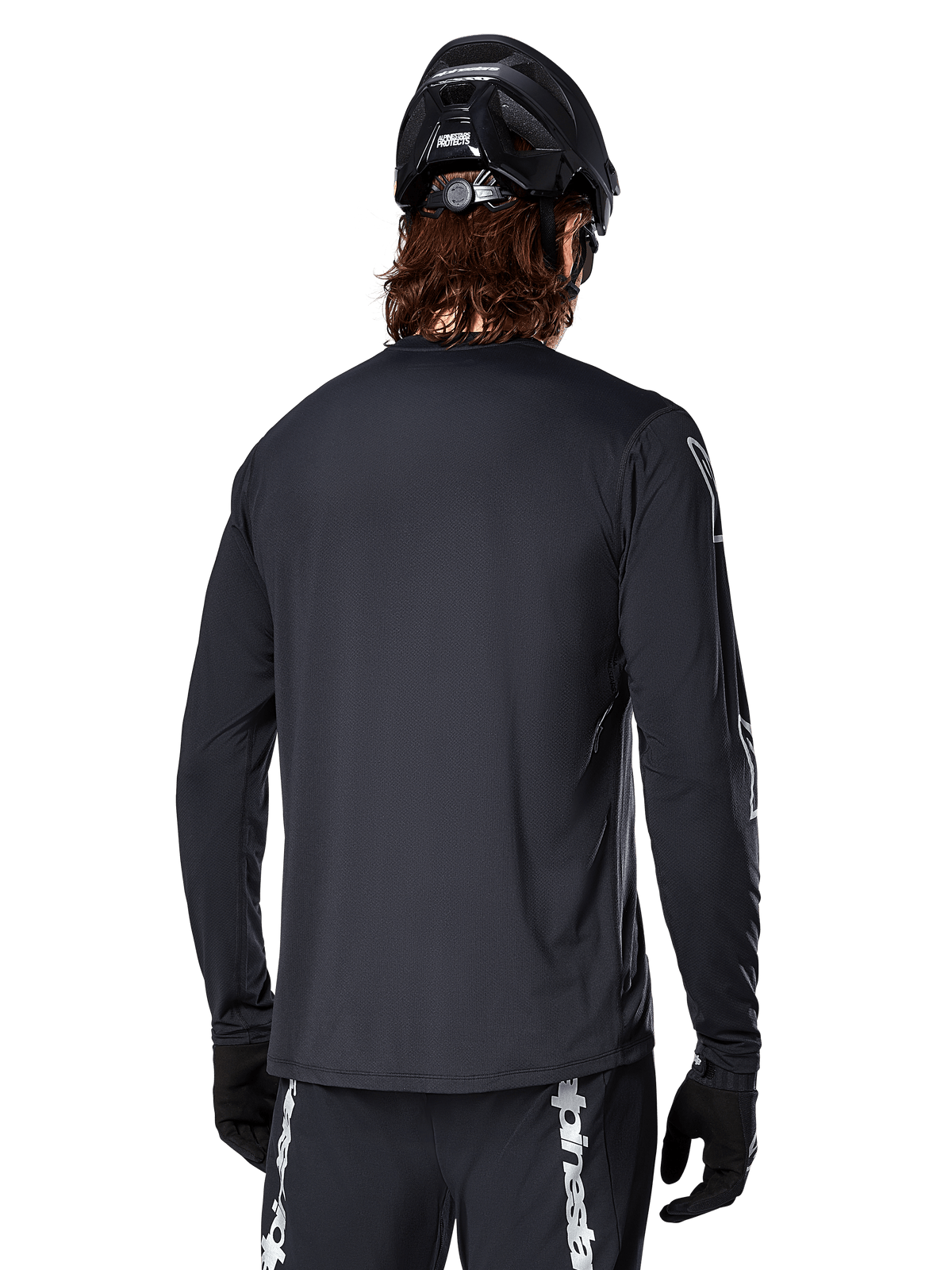 Alpinestars A-Dura Switch Long Sleeve Jersey, Black, rear view on a cyclist wearing a black MTB helmet and gloves, featuring technical jacquard fabric and a drop tail for off-road riding