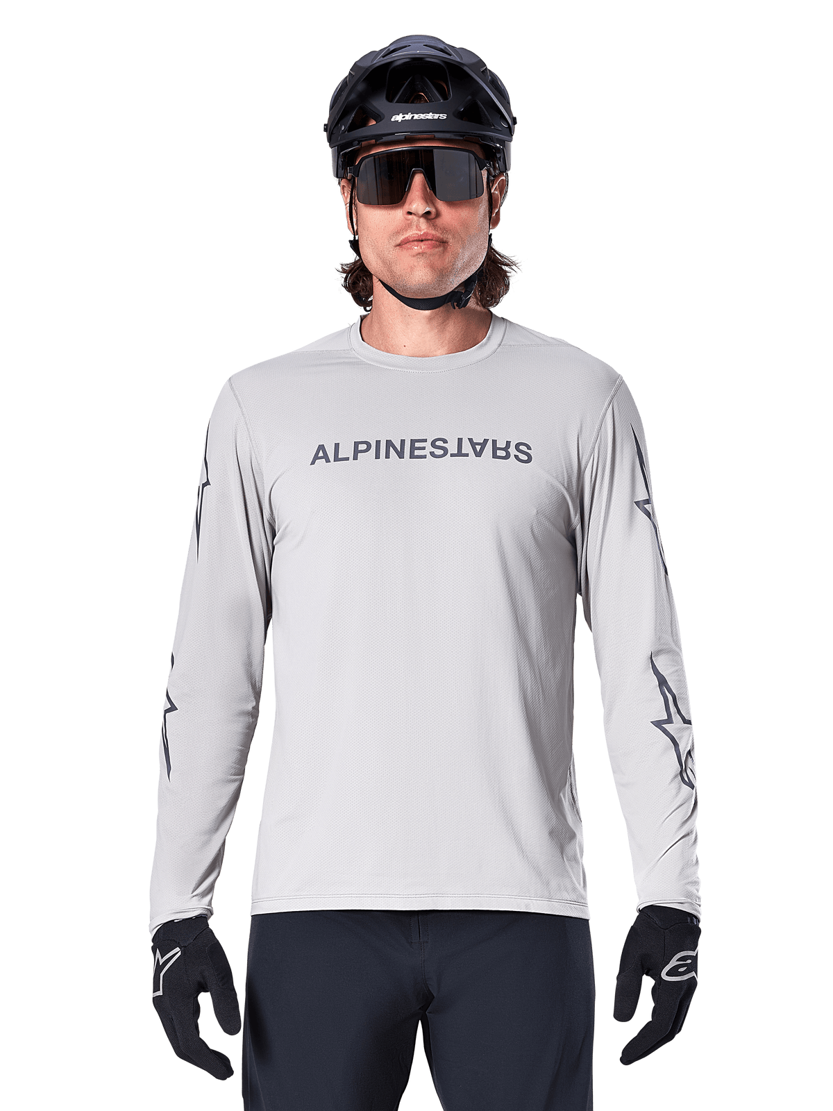 Alpinestars A-Dura Switch Long Sleeve Jersey, jasnoszara, posiada ciemnoszary napis na klatce piersiowej i logotypy gwiazdy na rękawach, noszona przez rowerzystę w czarnym kasku MTB i rękawiczkach, wydajna odzież rowerowa do jazdy po szlakach