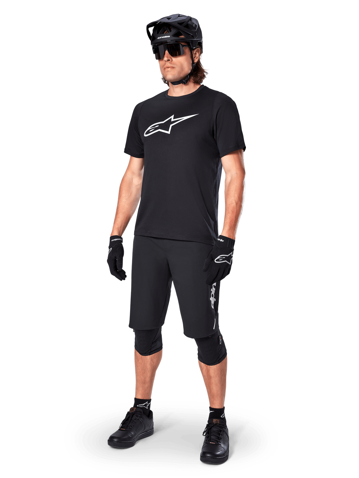 Mountain bike rider wearing the Alpinestars A-Dura Dri Oscar Short Sleeve Jersey in Black Reflective, featuring a large white logo on the chest, paired with matching black MTB shorts, gloves, and helmet, technical cycling apparel for off-road performance
