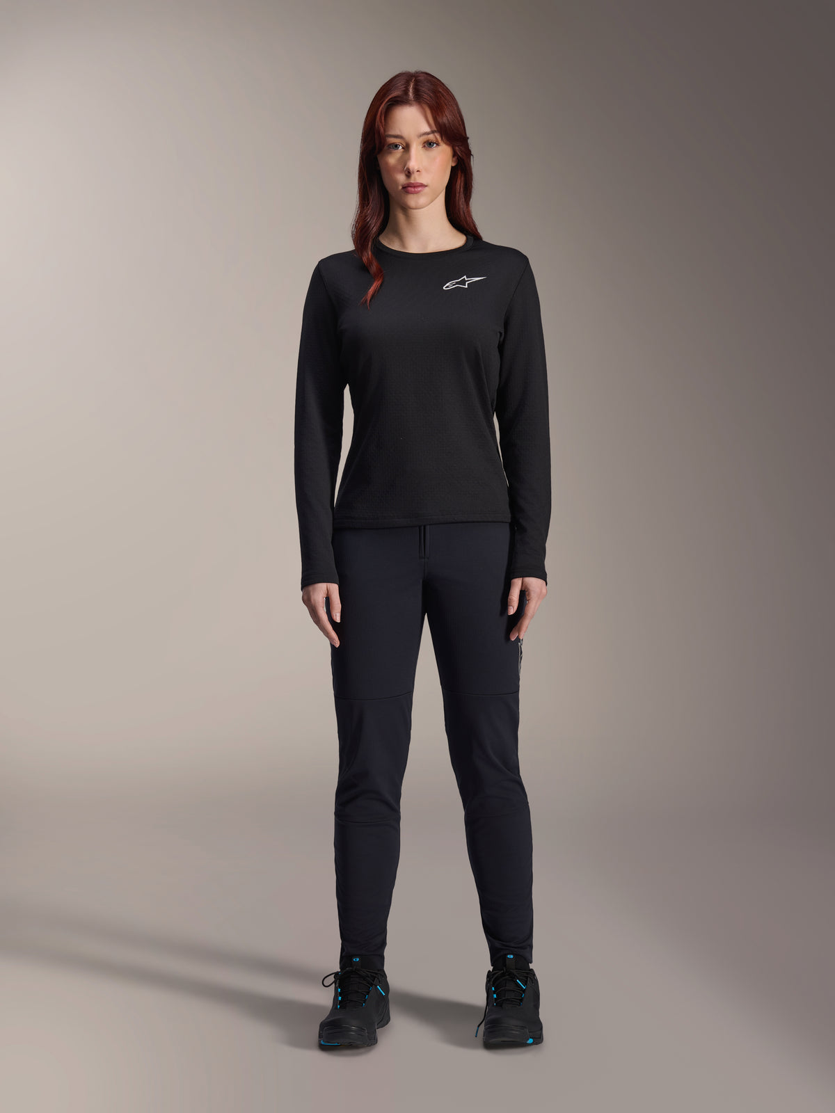 Alpinestars Stella A-Dura Thermal Jersey, damska koszulka rowerowa MTB z długim rękawem, czarna z białym logo na klatce piersiowej, noszona z dopasowanym czarnym strojem i butami rowerowymi, portret studyjny.