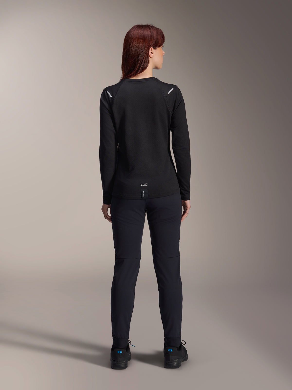 Alpinestars Stella A-Dura Thermal Jersey, damska koszulka rowerowa, widok z tyłu, czarna, ocieplany polar, długi rękaw, zestawiona z czarnymi spodniami i butami, logo A-Dura na dole pleców, odblaskowe detale na ramionach, przeznaczona do jazdy MTB