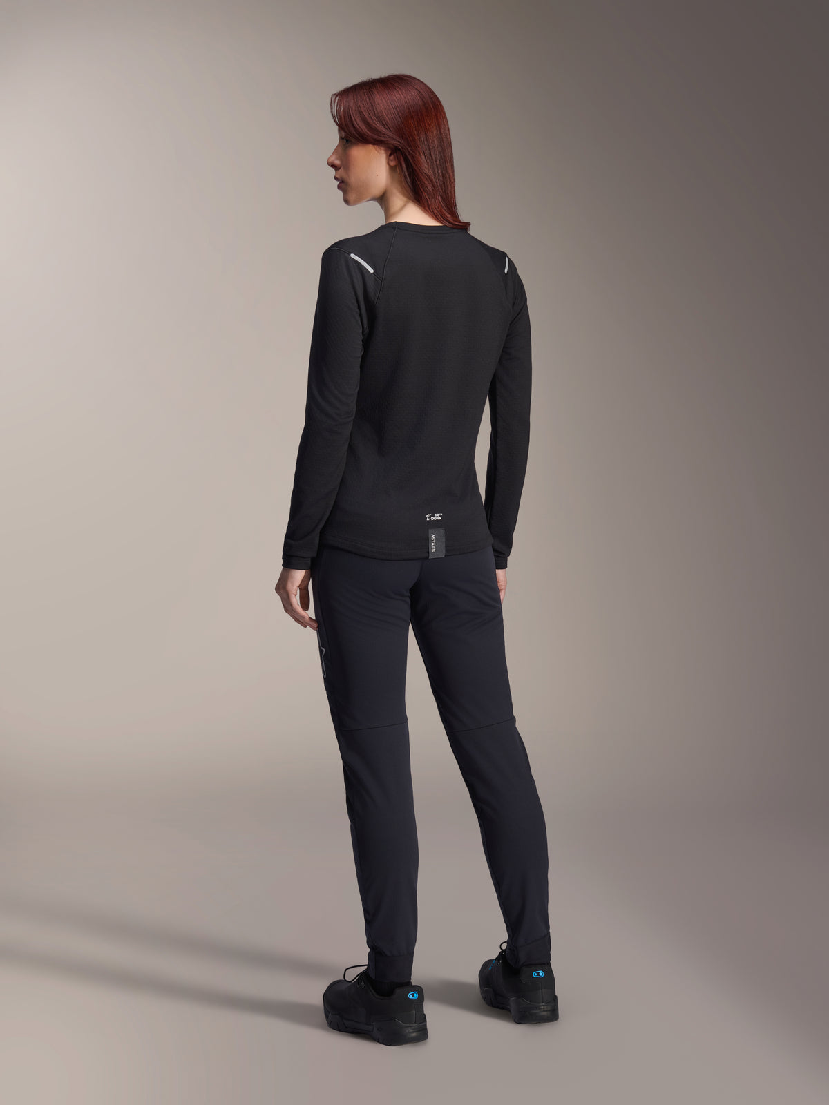 Alpinestars Stella A-Dura Thermal Jersey, damska koszulka MTB z długim rękawem w kolorze czarnym, widok z tyłu pokazujący odblaskowe akcenty na ramionach i przedłużony tył, noszona z czarnymi spodniami i butami, profesjonalna odzież do kolarstwa górskiego.