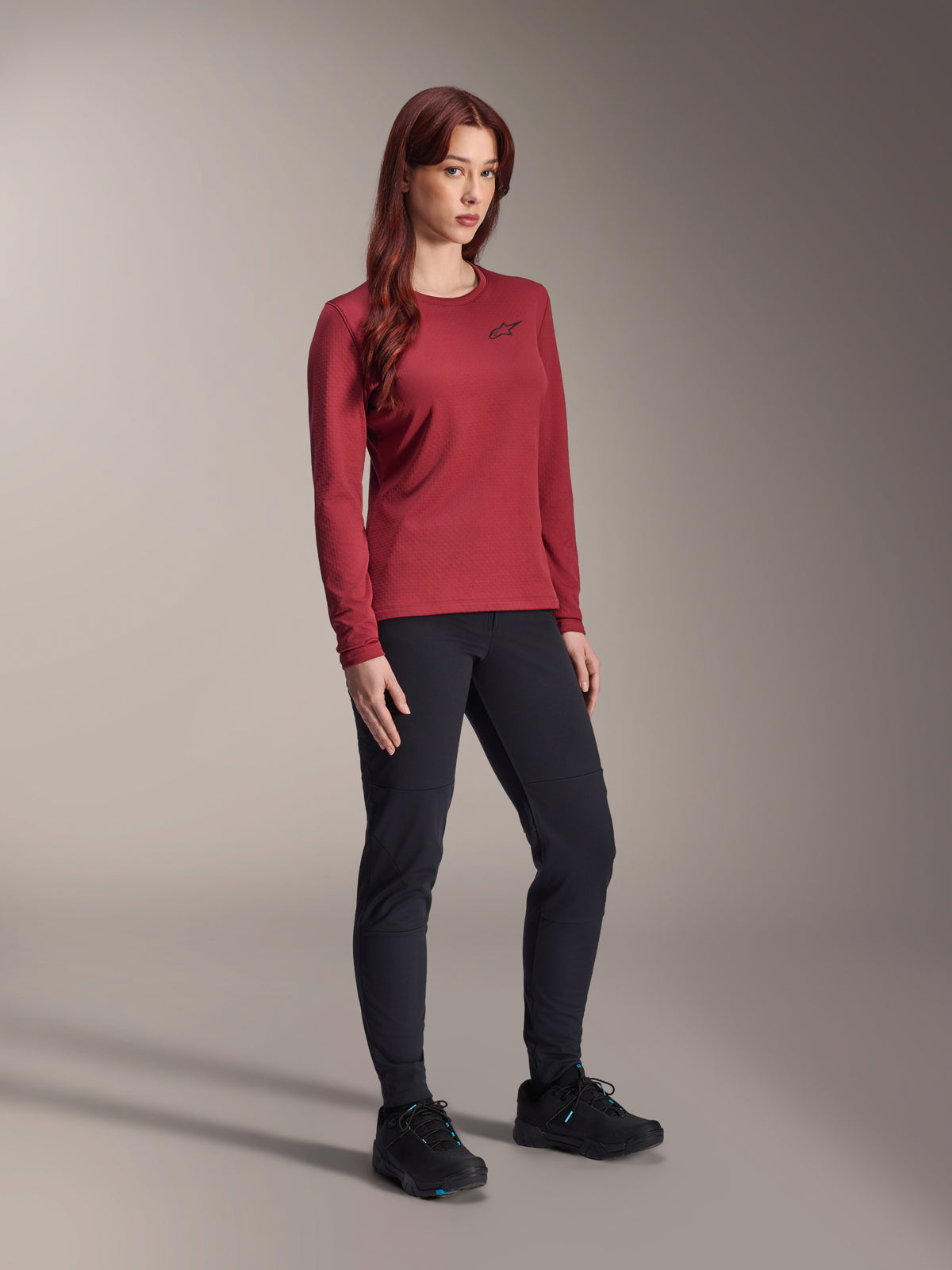 Woman wearing Alpinestars Stella A-Dura Thermal Pants in black and a maroon long-sleeved Stella A-Dura Thermal Jersey, technical mountain bike apparel for cold-weather riding, slim fit design with durable material, studio background