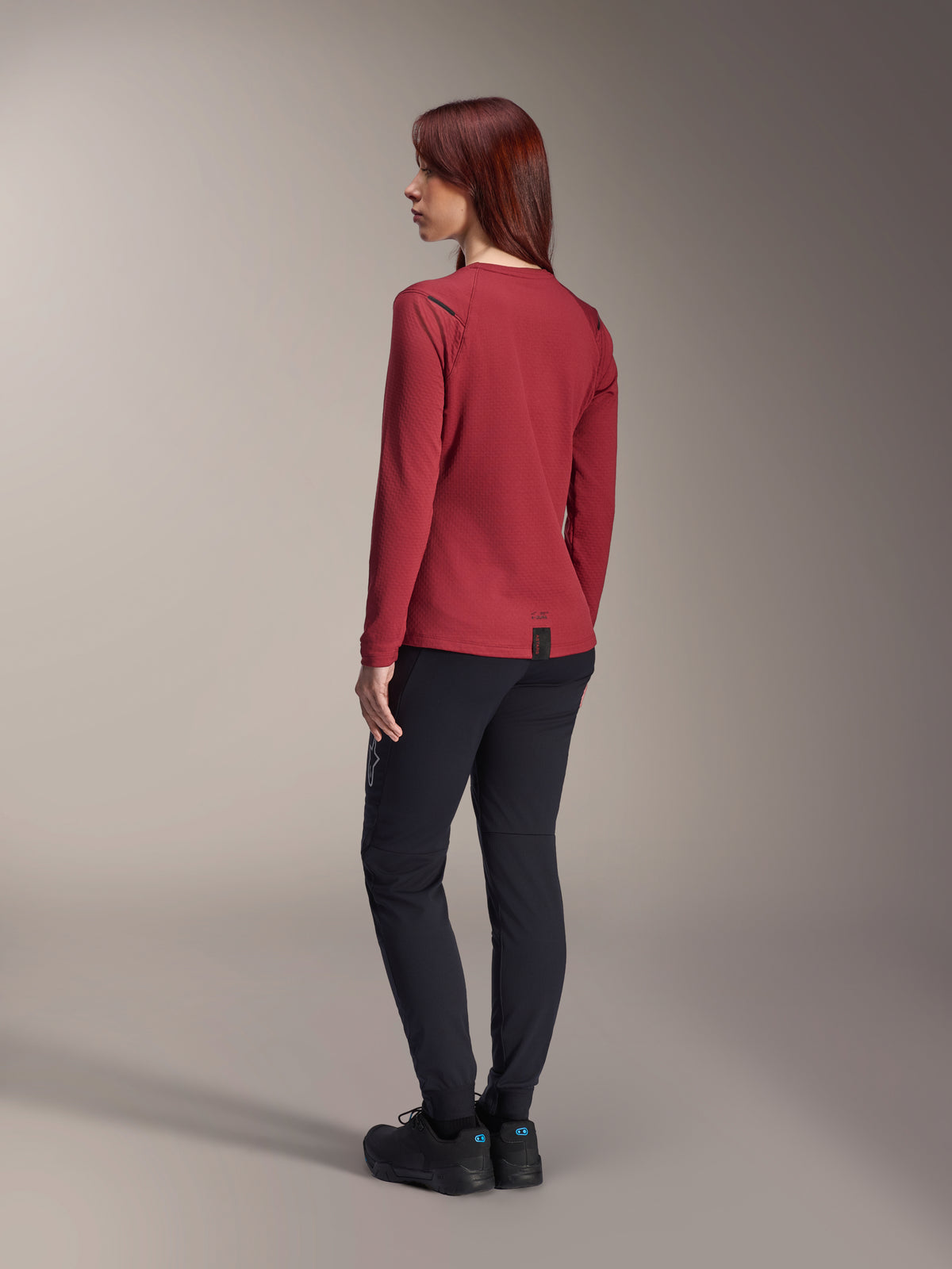 Woman wearing Alpinestars Stella A-Dura Thermal Pants in Black, paired with a red long-sleeve thermal jersey and black shoes, rear view, mountain bike apparel for cold-weather riding.