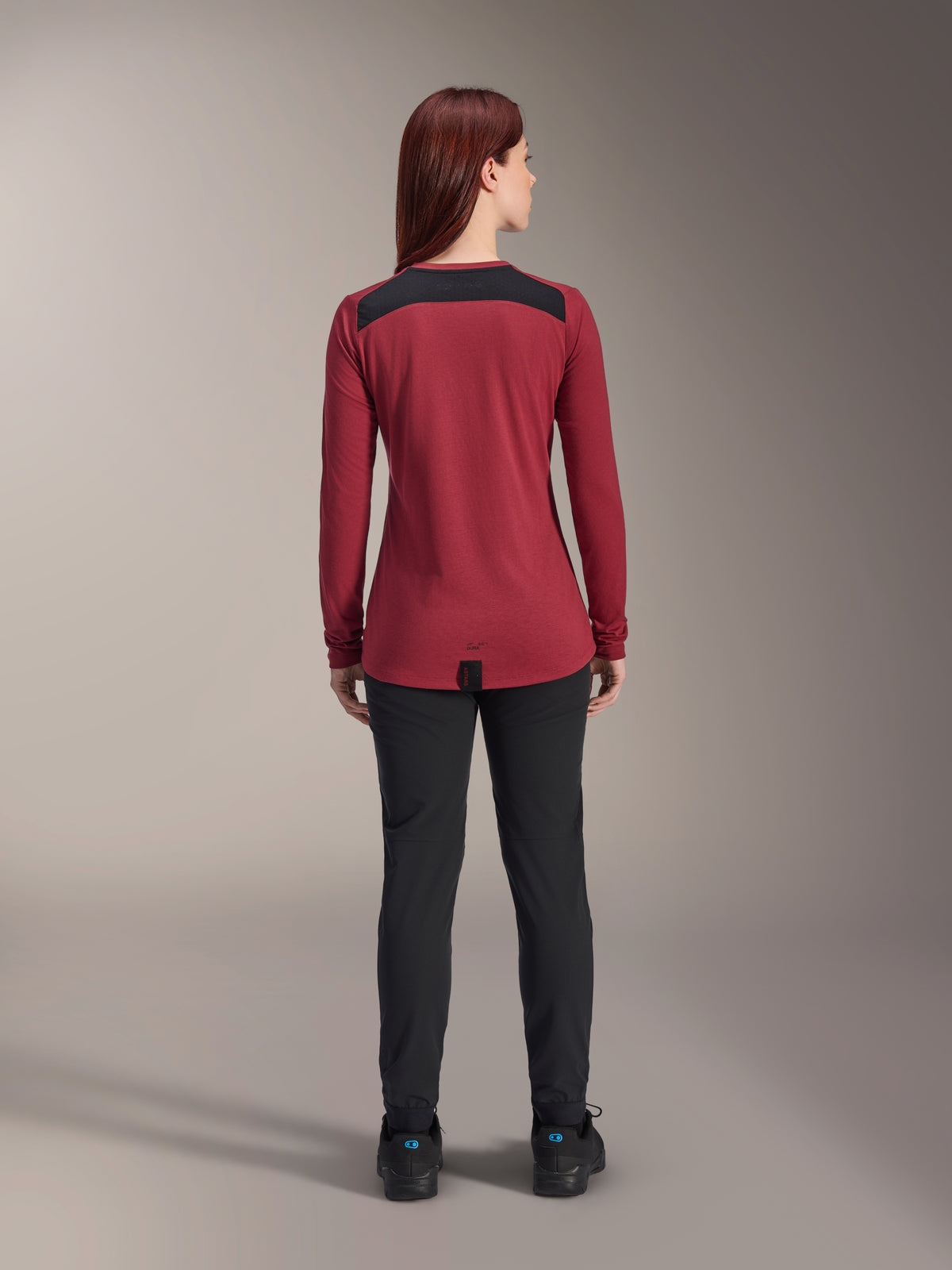 Alpinestars Stella A-Dura Dri Astar Long Sleeve Jersey, damska koszulka z długim rękawem, bordowa z czarnymi siatkowymi panelami na ramionach, techniczna odzież MTB widoczna od tyłu z czarnymi spodniami, wydłużony tył zapewniający osłonę podczas jazdy