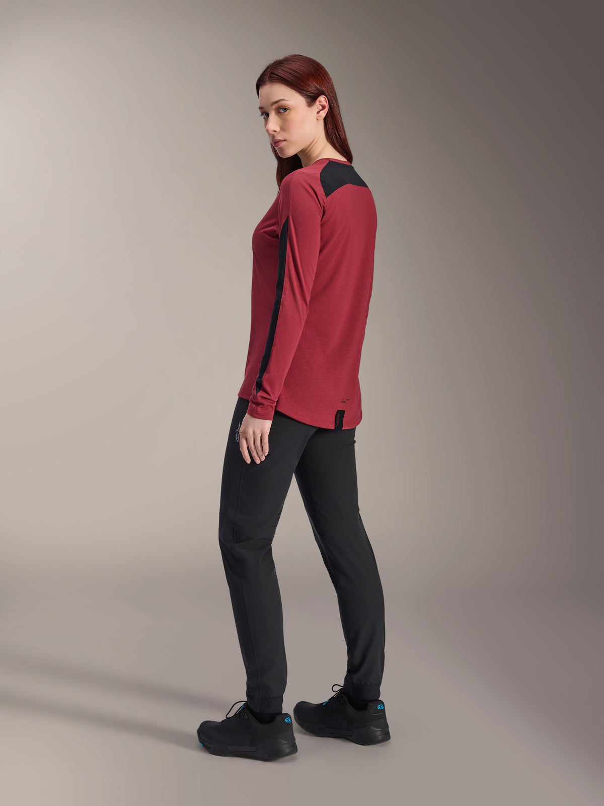 Damska koszulka Alpinestars Stella A-Dura Dri Astar Long Sleeve, bordowo-czarna, noszona z czarnymi spodniami MTB i czarnymi butami, widok z profilu z tyłu, recyklingowa tkanina drirelease z panelami z siatki, techniczna odzież na rower górski