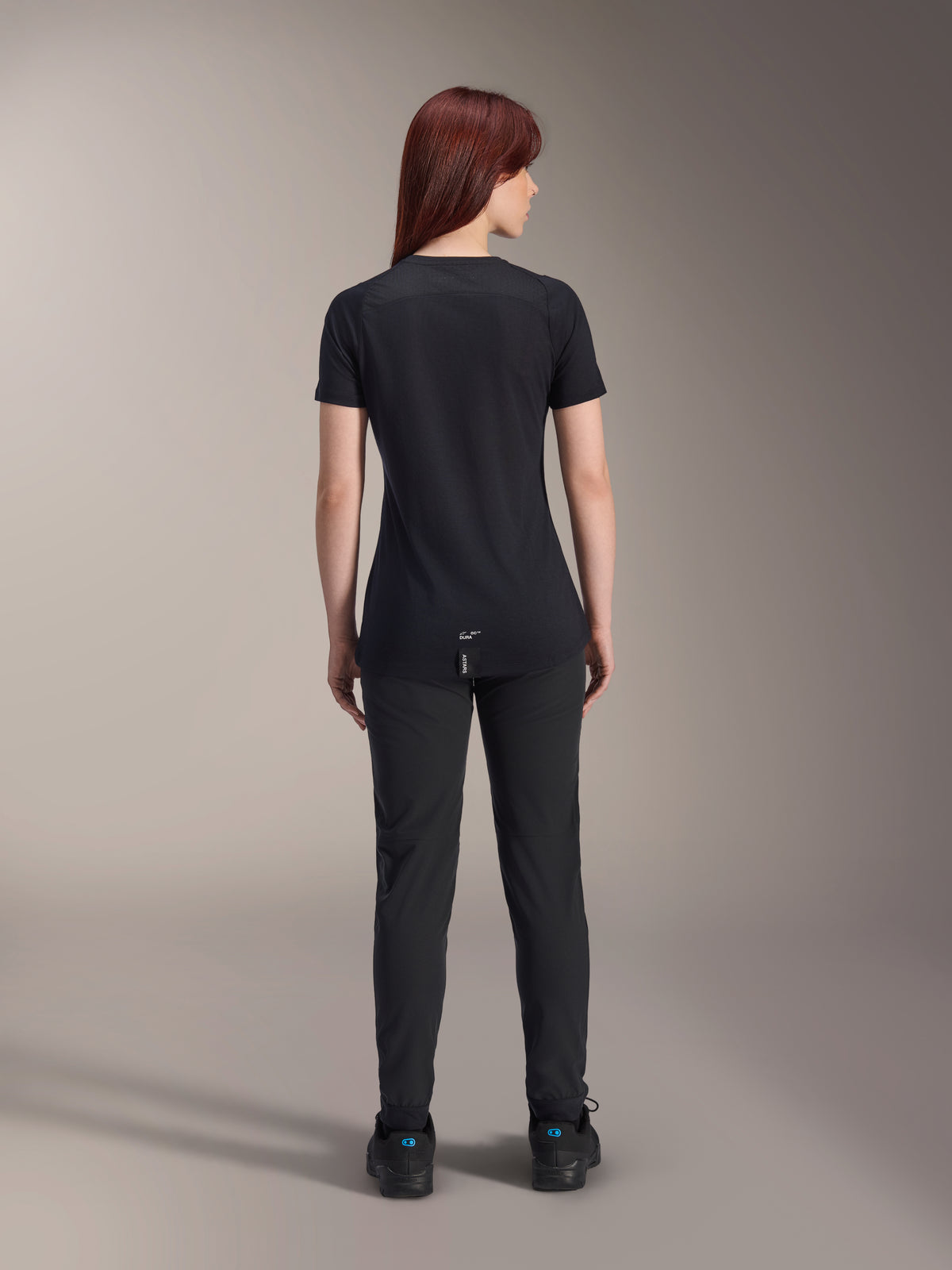 Alpinestars Stella A-Dura Dri Switch Jersey, damska koszulka rowerowa z krótkim rękawem, czarna, widok z tyłu na modelce, przedłużony tył i techniczne panele z siatki, czarne spodnie, wyczynowa odzież MTB