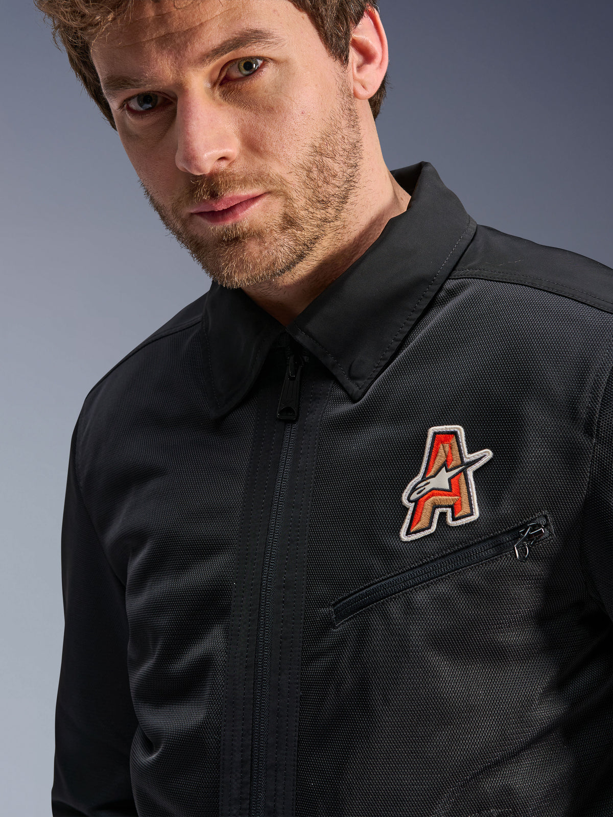 Kurtka Alpinestars Ignite Air, czarna, z tradycyjnym kołnierzykiem koszulowym i oddychającą siatkową konstrukcją, z czerwono-złotą naszywką z logo „A” na piersi, prezentowana na modelu, miejska odzież motocyklowa