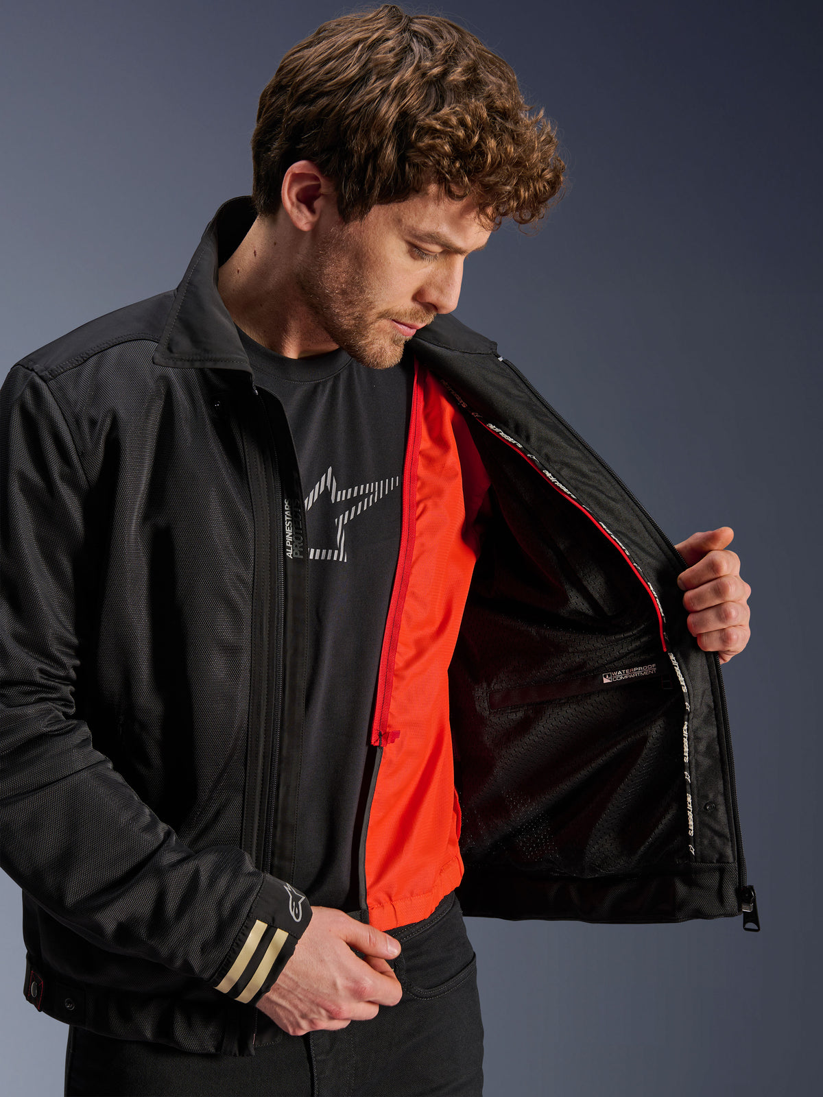 Alpinestars Ignite Air Jacket, czarna miejska kurtka motocyklowa, jaskrawopomarańczowa odpinana podpinka wiatroodporna, siatkowy korpus, widok wnętrza z wodoodporną przegrodą, czarny t-shirt z logo Alpinestars