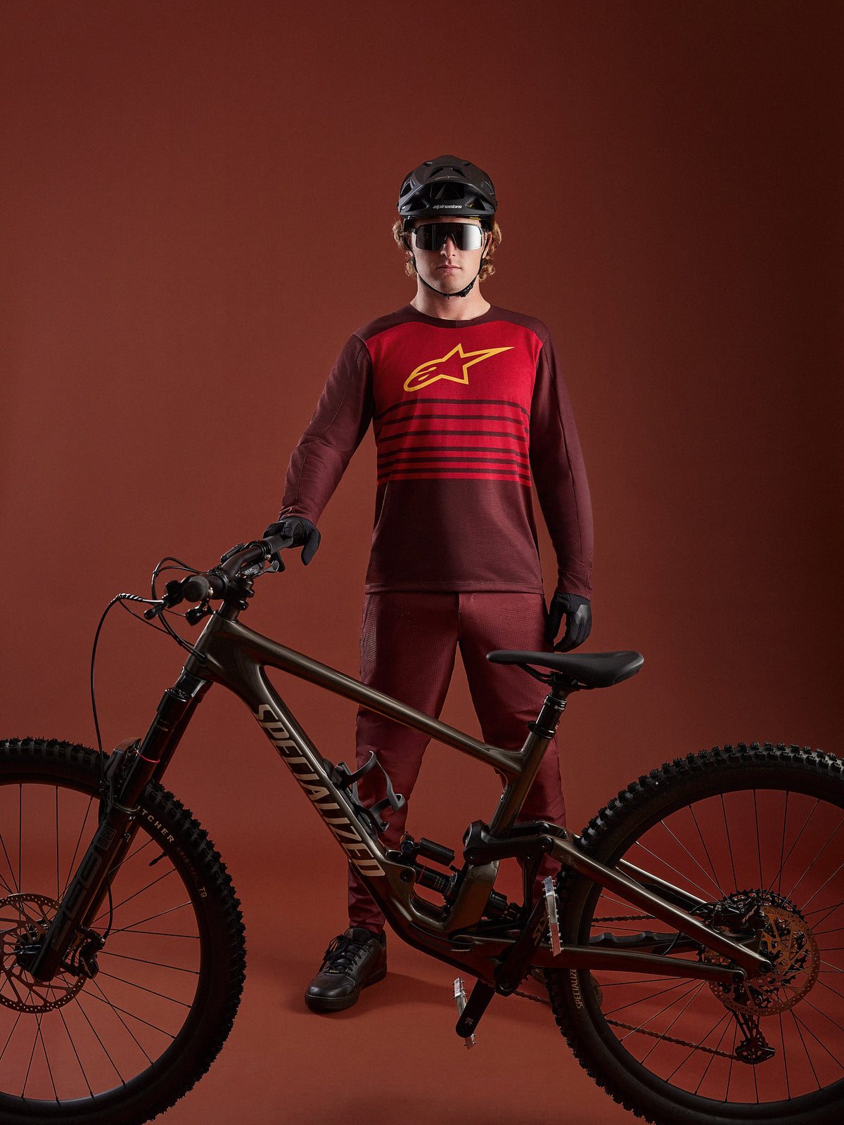 Bordowa koszulka MTB A-Dura Elite 2.0 z długim rękawem, czerwonym panelem i żółtym logo przy rowerze górskim.