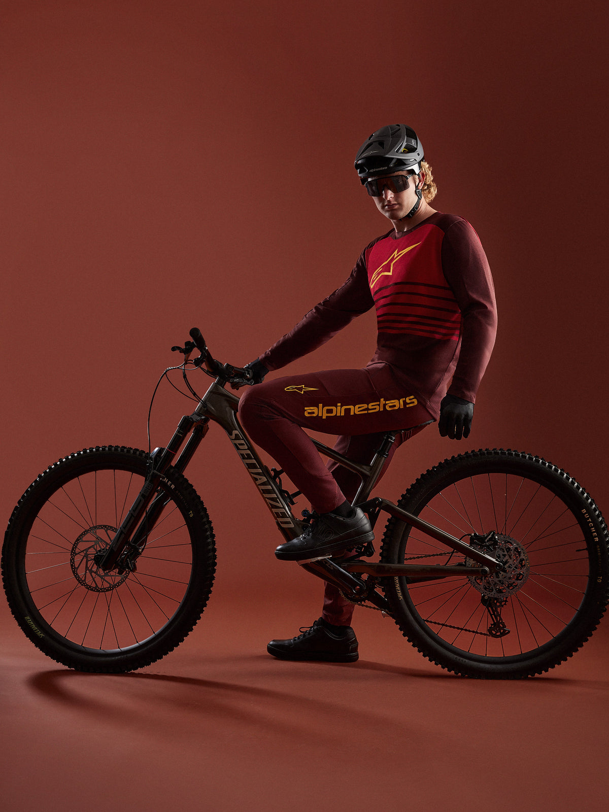 Zestaw Alpinestars A-Dura Elite 2.0 Bordeaux, koszulka i spodnie MTB, rowerzysta na rowerze Specialized w studiu.