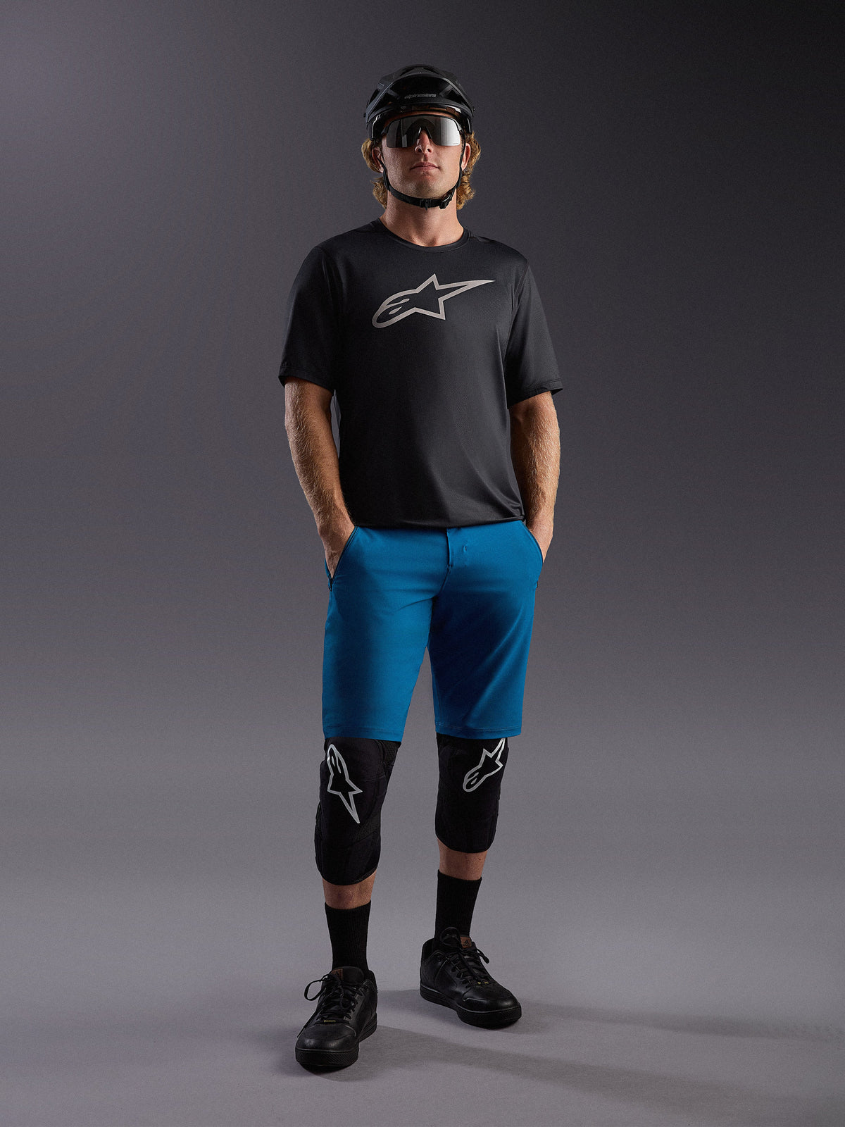 Koszulka Alpinestars A-Dura Ride SS i niebieskie szorty, kompletny strój MTB z ochraniaczami i kaskiem.