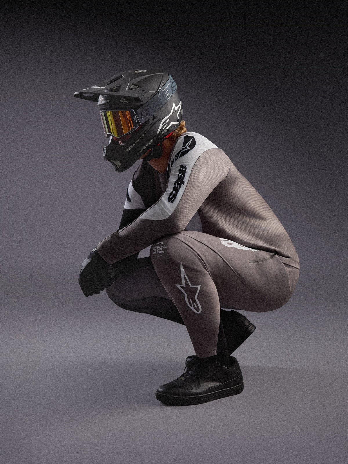 Szara, cieniowana koszulka i spodnie MTB A-Supra Elite, czarny kask full-face i gogle w stylizacji wyścigowej.