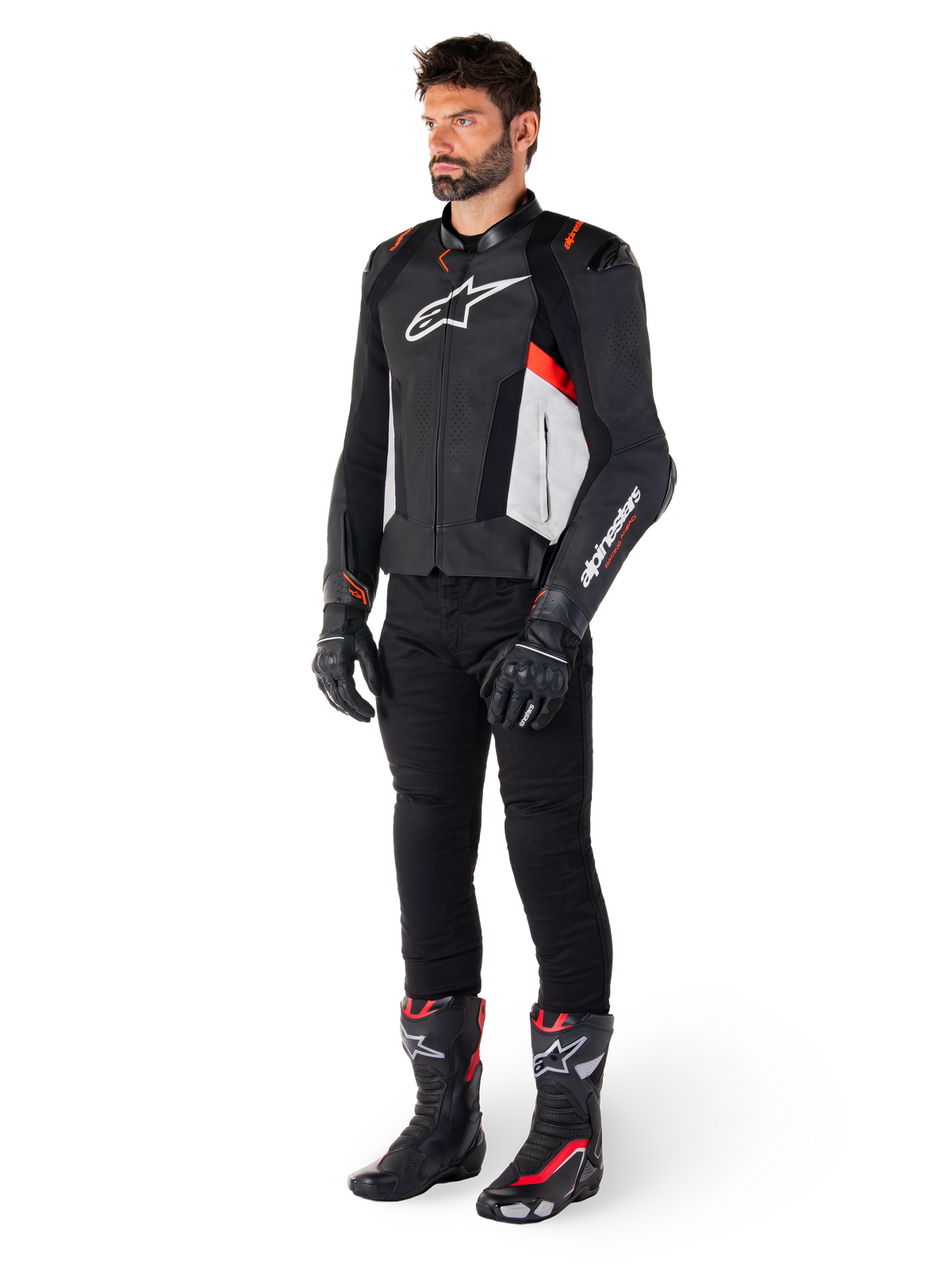 Męski model w skórzanej kurtce Alpinestars Missile V3, kolorystyka czarno-biało-czerwona (Red Fluo), czarne spodnie motocyklowe, rękawice i buty, konstrukcja z wysokiej jakości skóry bydlęcej, widoczne logo Alpinestars, profesjonalna sportowa estetyka wyścigowa