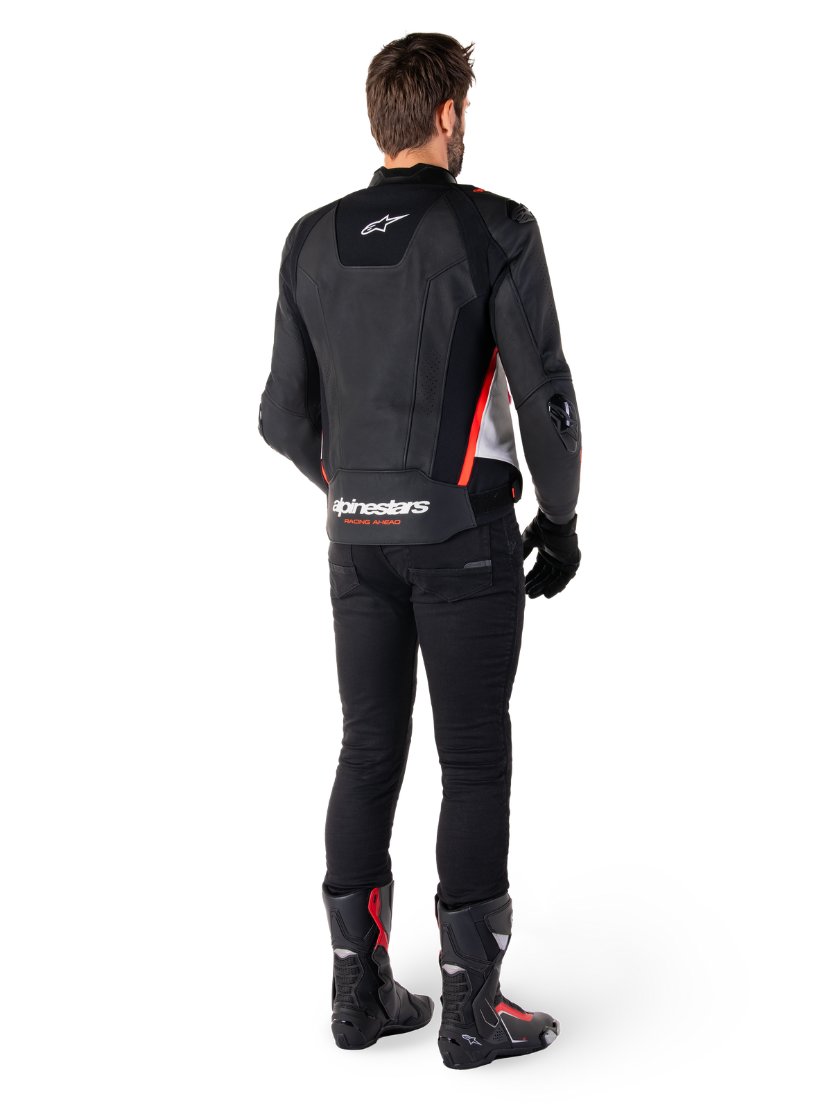 Skórzana kurtka Alpinestars Missile V3 w kolorze Black White Red Fluo, widok z tyłu na motocykliście, logo Alpinestars w górnej i dolnej części pleców, zestawiona z czarnymi spodniami i butami motocyklowymi, sportowa kurtka skórzana inspirowana wyścigami.