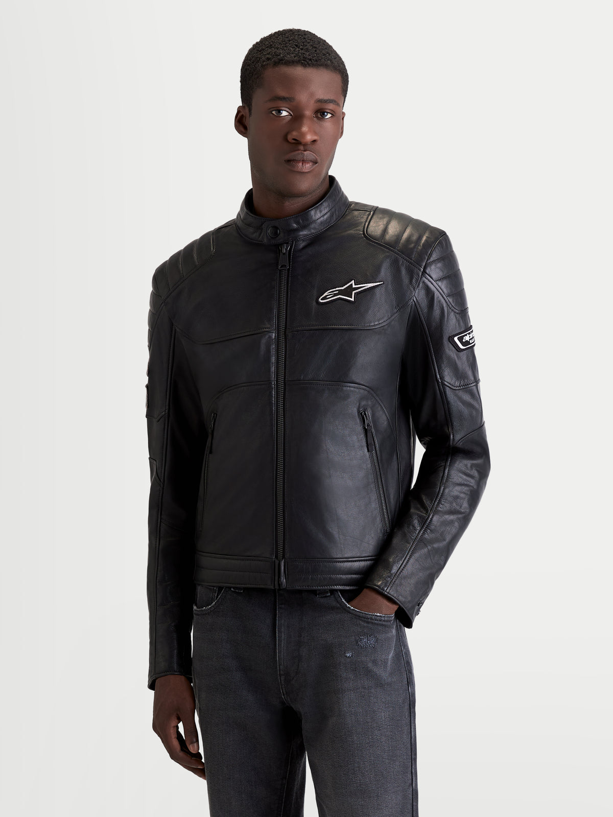 Alpinestars Revern Kurtka skórzana męska urban motocyklowa w kolorze czarnym, widok z przodu na modelu w odzieży heritage road z certyfikowaną ochroną ramion i łokci