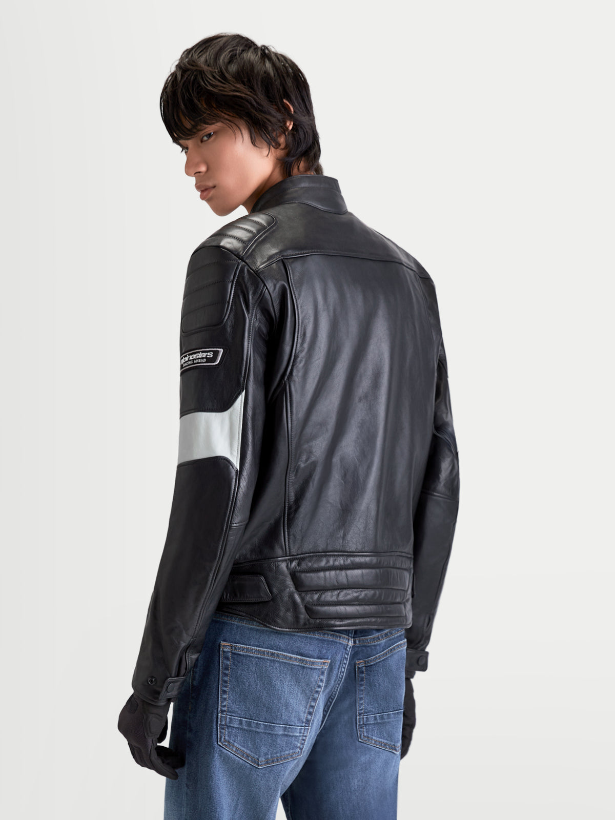 Alpinestars Revern Kurtka skórzana, męska urbanistyczna kurtka motocyklowa w kolorze czarnym i szarym, widok z tyłu na model w jeansach, prezentująca konstrukcję ze skóry licowej i klasyczny styl