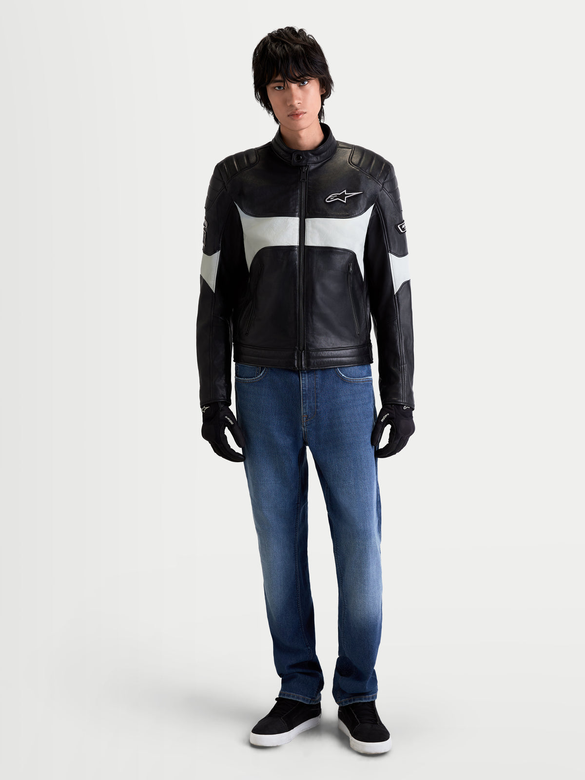 Alpinestars Revern Kurtka skórzana, męska motocyklowa kurtka skórzana w kolorze czarnym i metalicznym szarym, widok z przodu na modela ubranego w jeansy i czarne rękawice, prezentująca styl dziedzictwa i konstrukcję ze skóry licowej