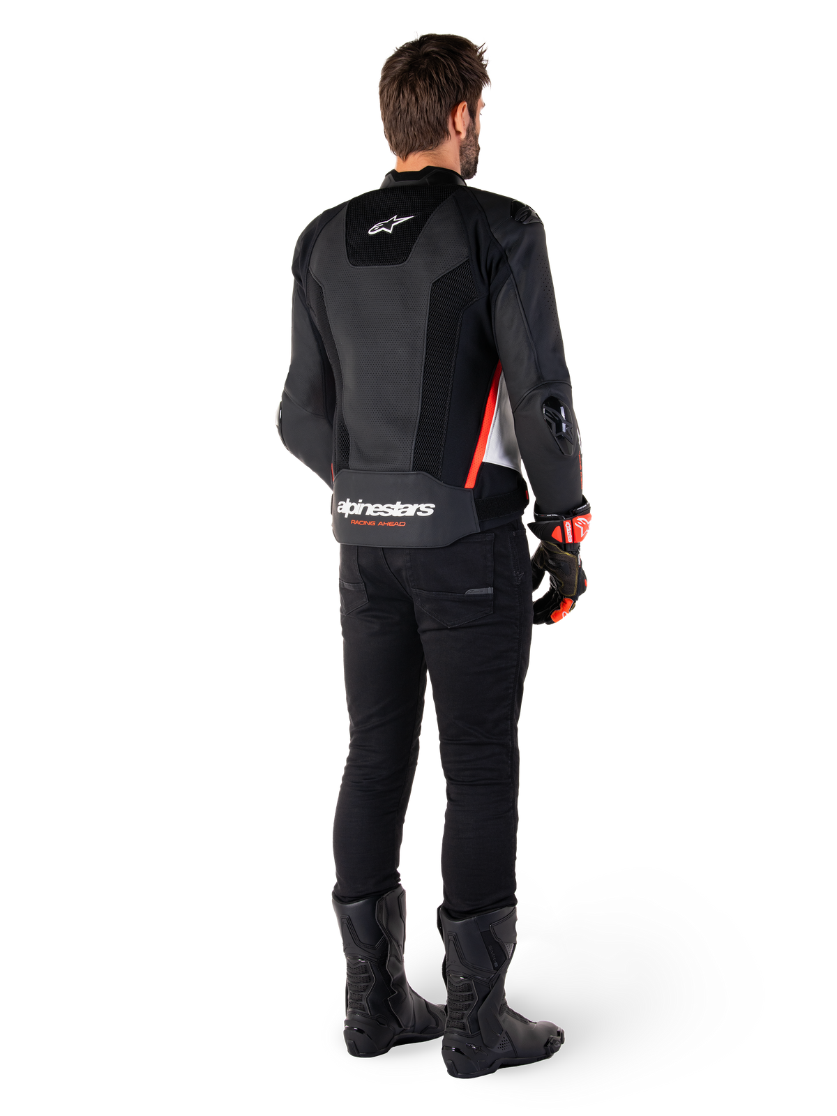Motocyklista widziany od tyłu w skórzanej kurtce Alpinestars Missile V3 Airflow w kolorze Black White Red Fluo, w zestawieniu z czarnymi spodniami i butami, z obszerną perforacją skóry dla wentylacji, ochraniaczami ramion DFS i wyraźnym logo Alpinestars na dolnej części pleców.