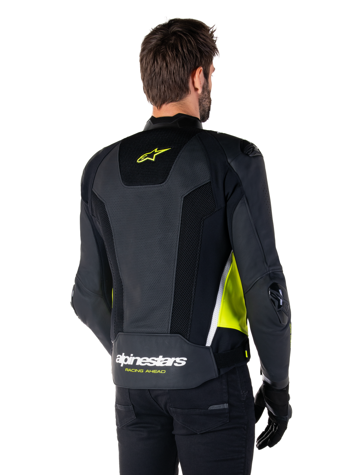 Skórzana kurtka Alpinestars Missile V3 Airflow, widok z tyłu na modelu, czarna z neonowożółtymi i białymi akcentami, posiada obszerne panele z perforowanej skóry i siatki na plecach, żółte logo gwiazdy oraz biały napis „RACING AHEAD”, zestawiona z czarnymi rękawicami i spodniami.