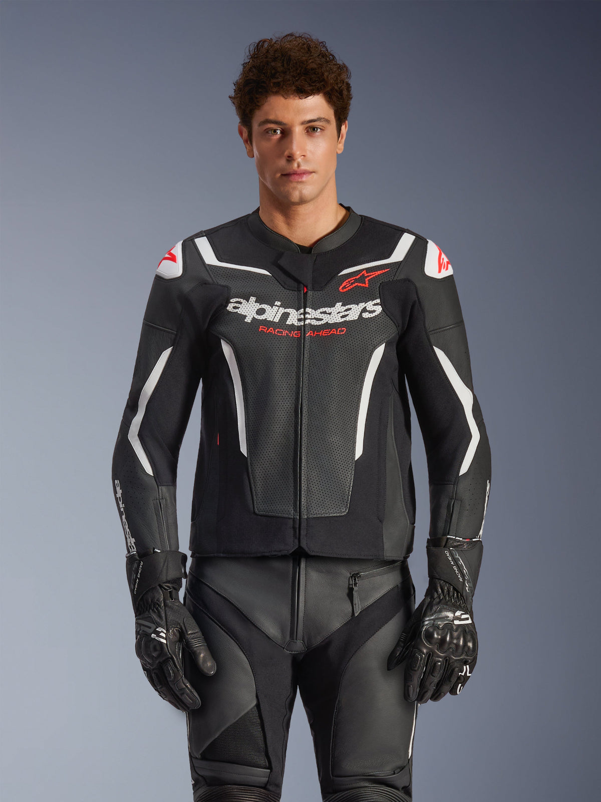 Skórzana kurtka Alpinestars GP Force V2 Air, czarna z białymi i czerwonymi akcentami, model w perforowanej kurtce skórzanej z logo „alpinestars” i napisem „RACING AHEAD” na klatce piersiowej, w zestawieniu z dopasowanymi spodniami wyścigowymi i rękawicami, sportowa odzież motocyklowa klasy premium