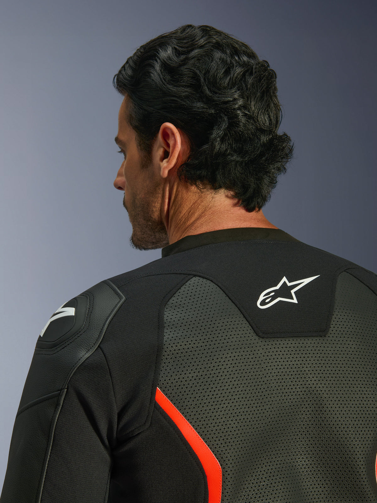 Skórzana kurtka Alpinestars GP Force V2 Air, czarna z czerwonymi akcentami fluo, zbliżenie na górną część pleców i ramię, liczne perforacje skóry dla przepływu powietrza, białe logo na plecach i ochrona ramion GP Lite Evo