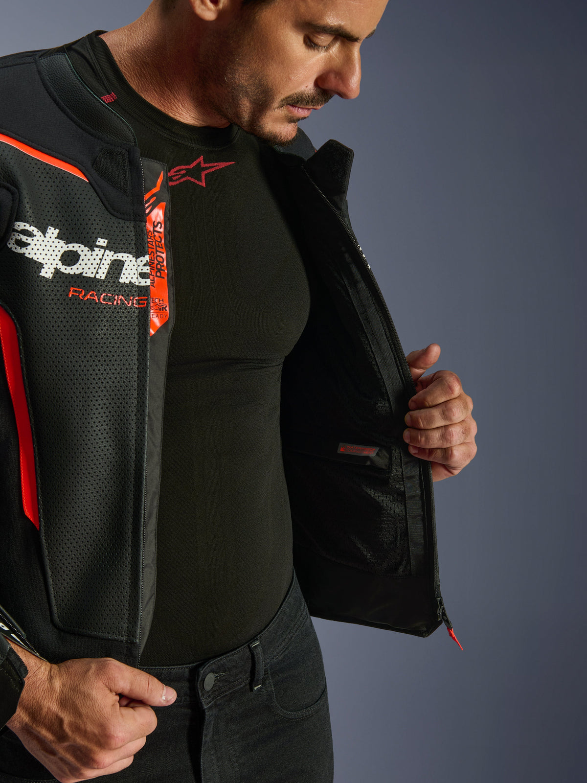 Alpinestars GP Force V2 Air Leather Jacket, czarno-czerwona (Red Fluo), rozpięta, ukazująca wewnętrzną wodoodporną kieszeń i branding, wielopanelowa konstrukcja z perforowanej skóry dla optymalnego przepływu powietrza, noszona z czarną warstwą bazową Alpinestars