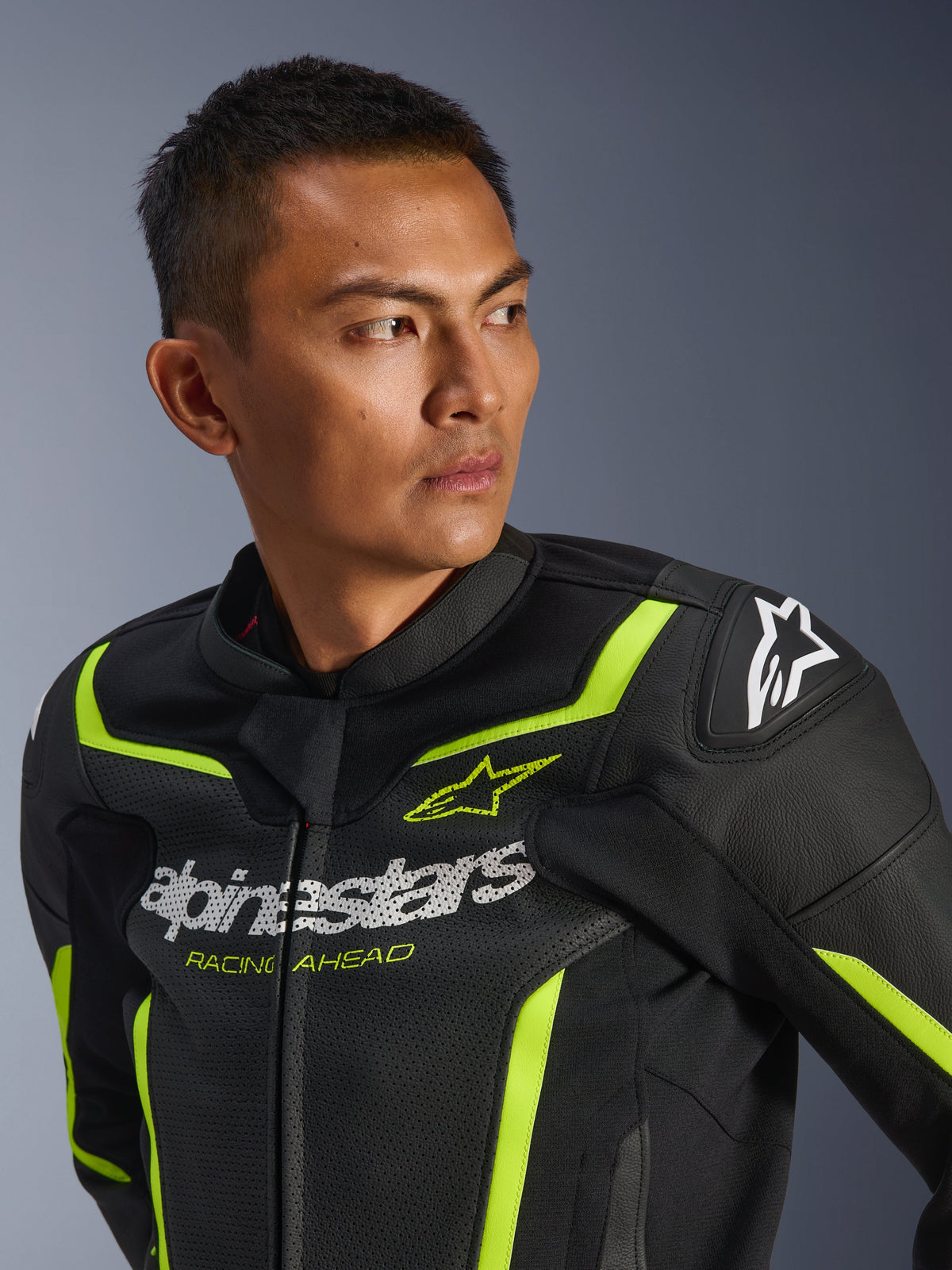 Alpinestars GP Force V2 Air Leather Jacket, perforowana sportowa kurtka motocyklowa, czarno-żółta fluo, białe logo na klatce piersiowej z napisem „Racing Ahead”, neonowe akcenty i ochronne slidery na ramionach, prezentowana przez modela.