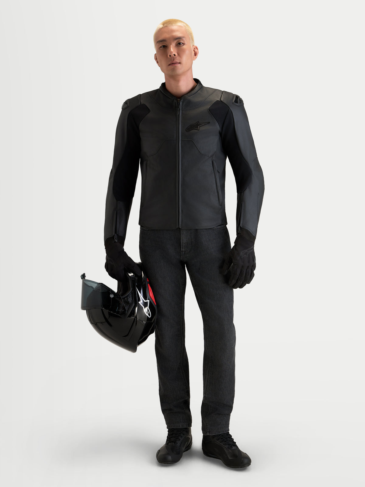 Alpinestars Caliber V2, męska czarna skórzana kurtka motocyklowa z certyfikatem AA, niskoprofilowymi ramionami DFS i konstrukcją z licowanej skóry bydlęcej, prezentowana na modelu trzymającym czarny kask