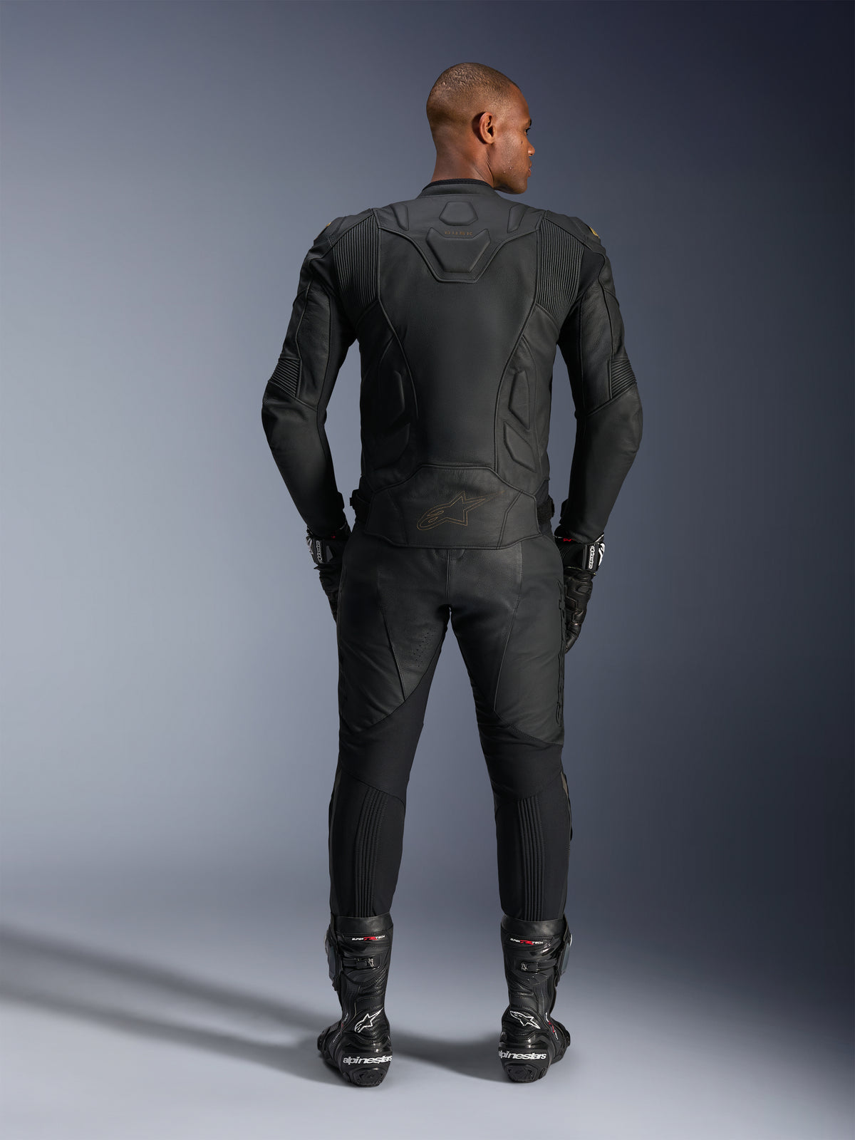 Alpinestars Dusk Leather Jacket, czarna wyścigowa kurtka ze skóry bydlęcej, widok z tyłu na motocykliście w pełnej ochronie.