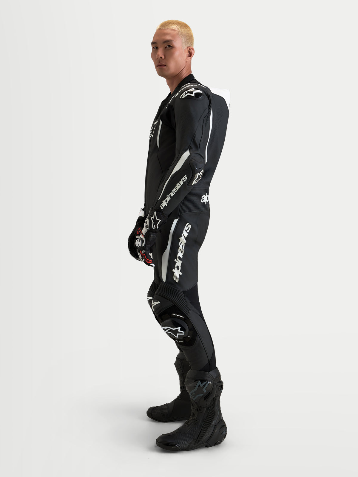 Alpinestars Missile V3 Leather Suit 1 Pc, męski jednoczęściowy skórzany kombinezon wyścigowy, czarno-biały, z aerodynamicznym garbem i ochroną CE, widok z boku na modelu.