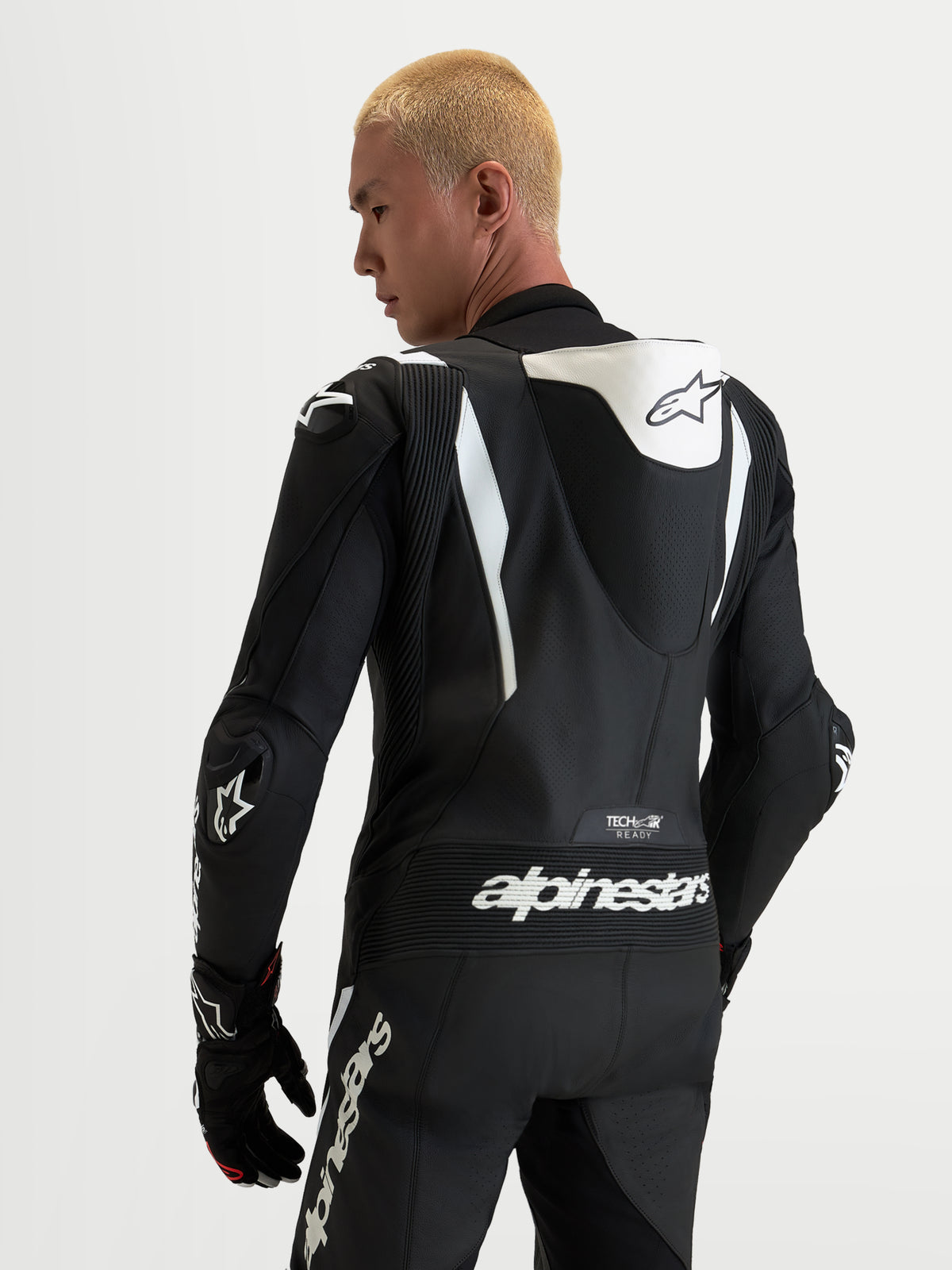 Alpinestars Missile V3, jednoczęściowy skórzany kombinezon motocyklowy, czarny i biały, z aerodynamicznym garbkiem, brandingiem Tech-Air ready oraz ochraniaczami ramion DFS, widok z tyłu na modelu.