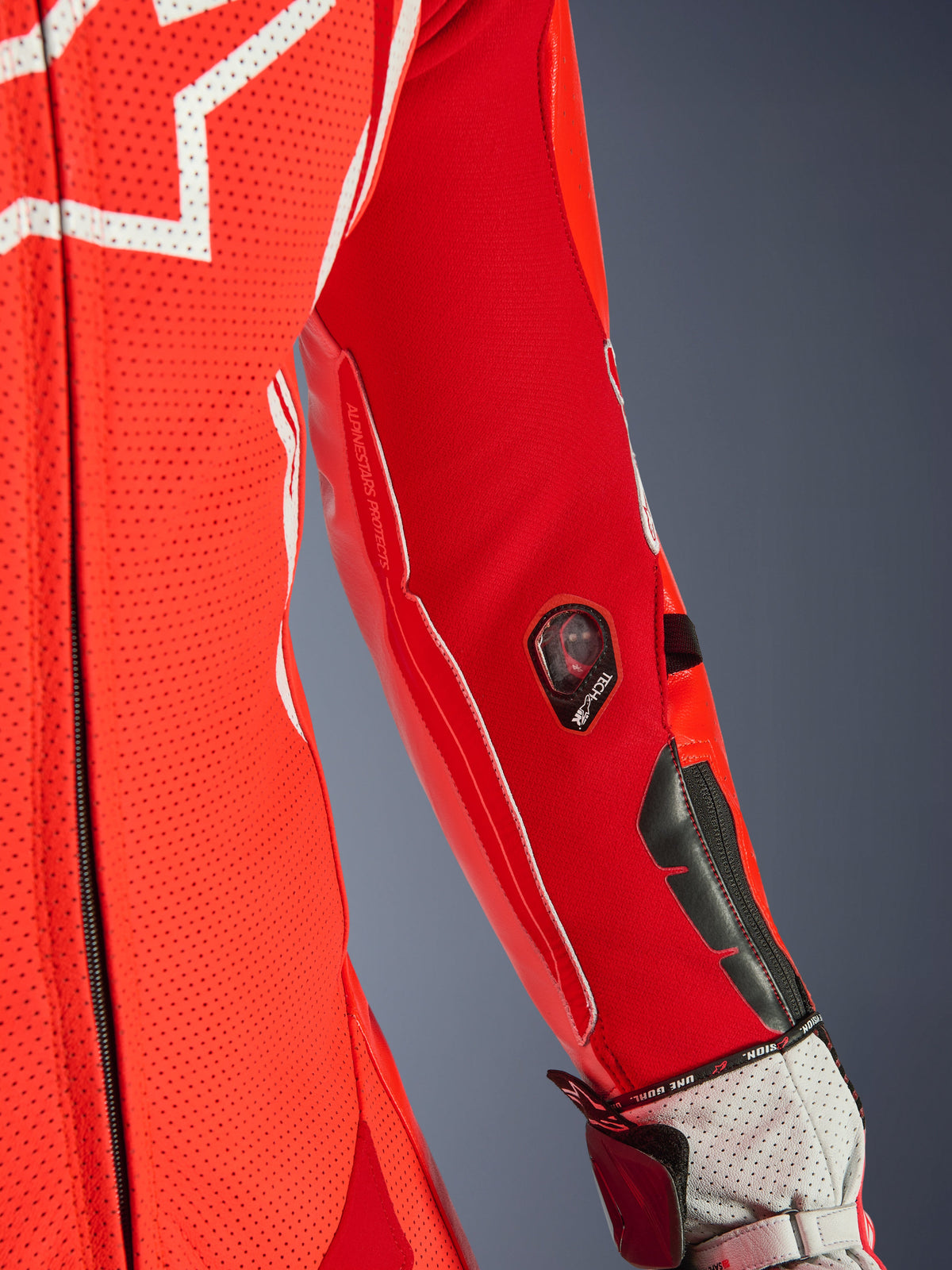 Alpinestars GP Tech V5 One Piece Leather Suit, czerwony fluorescencyjny i jasnoczerwony, zbliżenie na rękaw ze wskaźnikiem Tech-Air i ochronnymi sliderami, perforowana skóra z białymi akcentami, profesjonalny detal wyścigowy