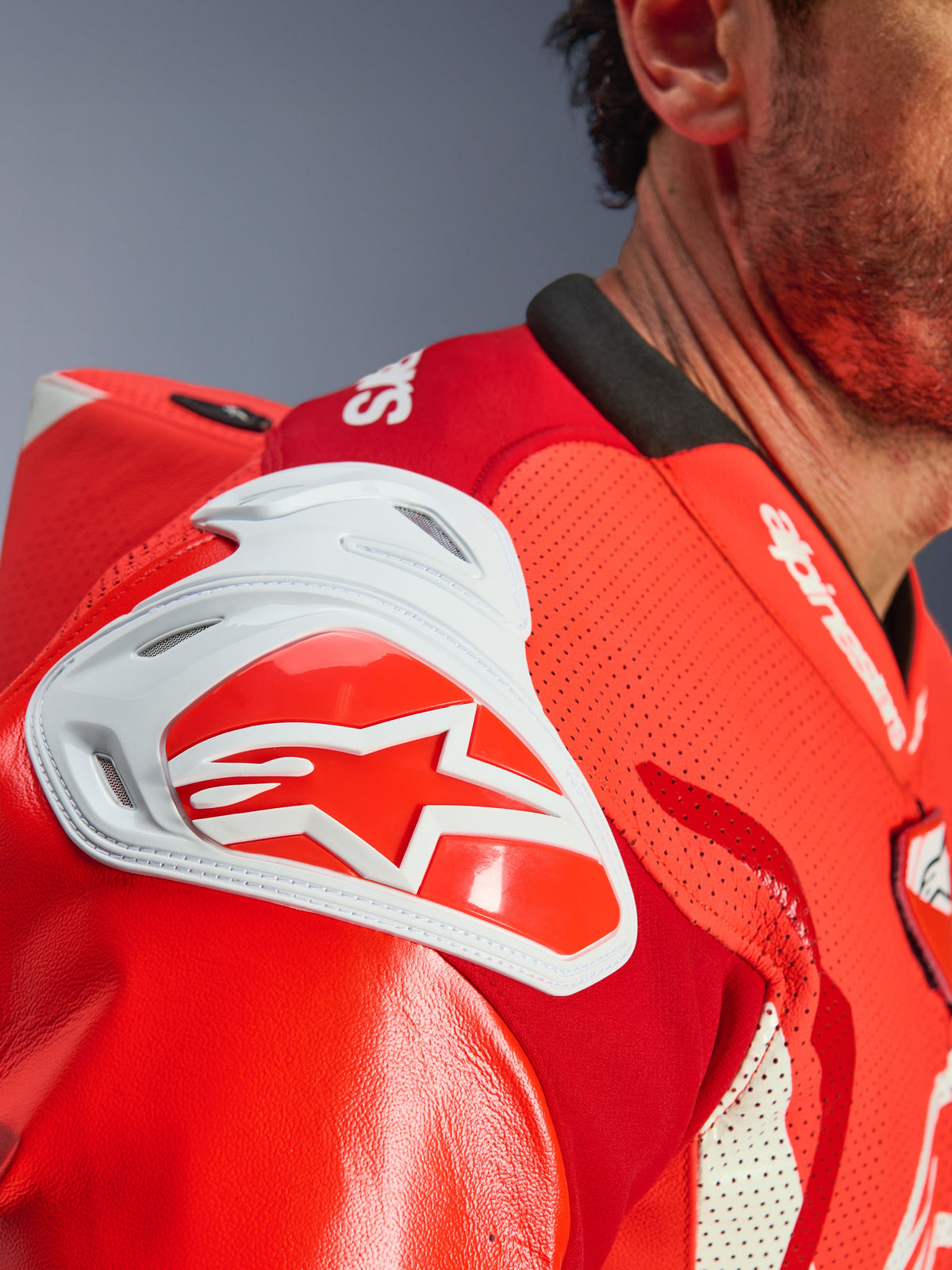 Alpinestars GP Tech V5 One Piece Leather Suit, zbliżenie na obszar barku, kolor czerwony fluo i jaskrawy czerwony, biały ochraniacz GP DFS z czerwonym logo gwiazdy, perforowana skóra zapewniająca wentylację