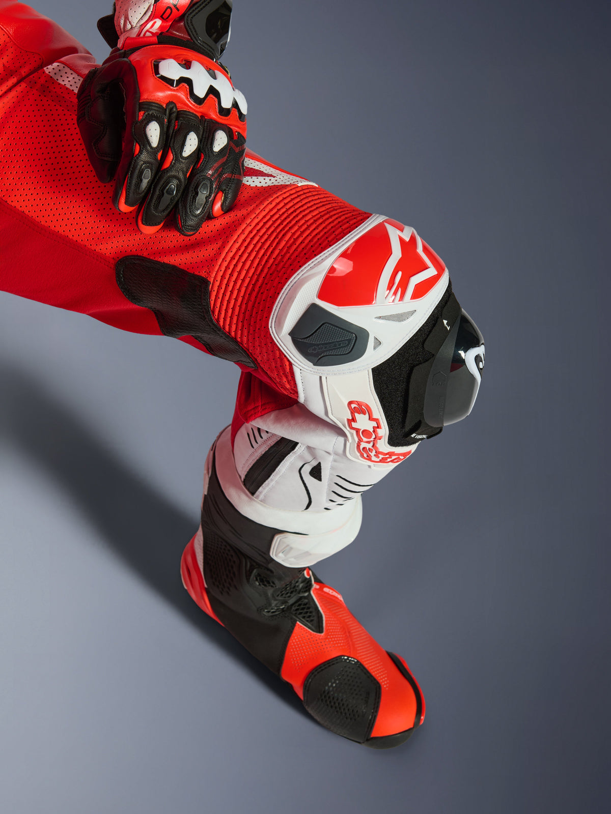 Alpinestars GP Tech V5 One Piece Leather Suit, jednoczęściowy kombinezon skórzany, czerwony fluo, jaskrawoczerwony i biały, zbliżenie na nogę z ochraniaczem kolana i sliderem, perforowana skóra i elastyczne panele akordeonowe, w komplecie z pasującą rękawicą i butem wyścigowym