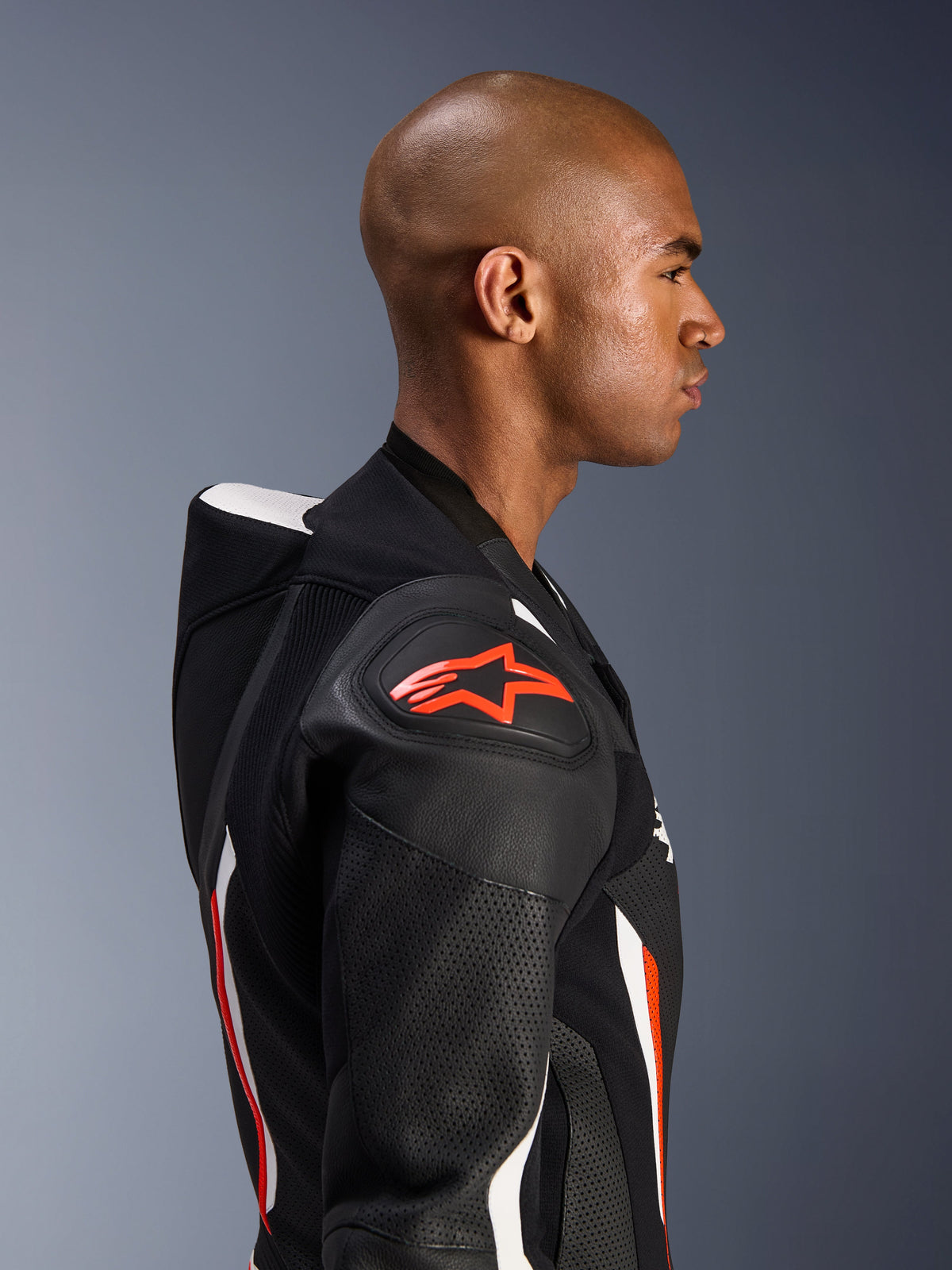 Alpinestars GP Force V2 Leather Suit - 1Piece, side profile of a rider, Black White Red Fluo colorway, highlighting the aerodynamic speed hump, perforated leather zones, and DFS Lite shoulder protection with red Alpinestars logo