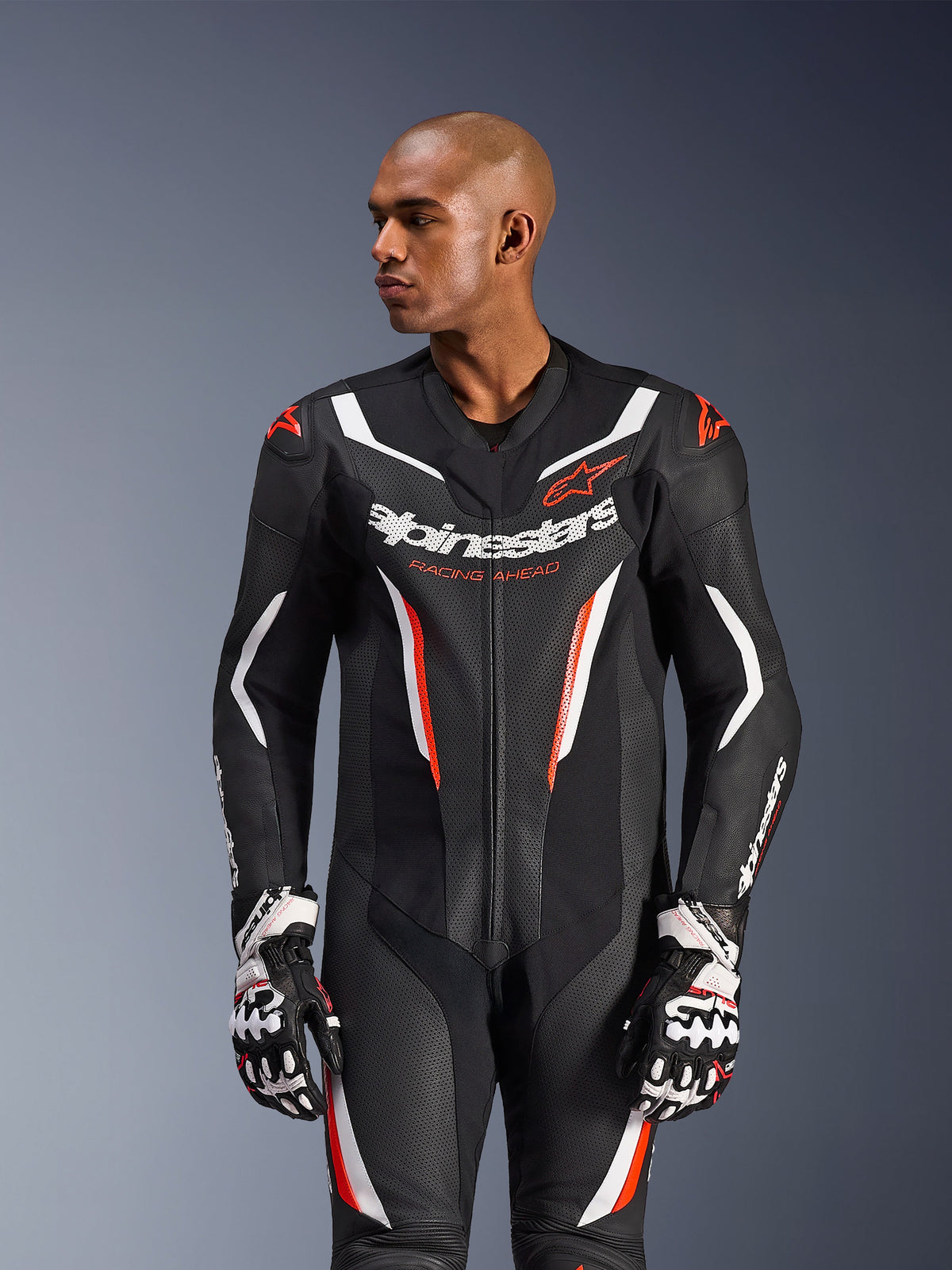 Alpinestars GP Force V2 Leather Suit 1-Piece, Black White Red Fluo, worn by a male model with racing gloves, featuring perforated leather construction, bold white and red graphic accents, and Alpinestars branding on the chest.